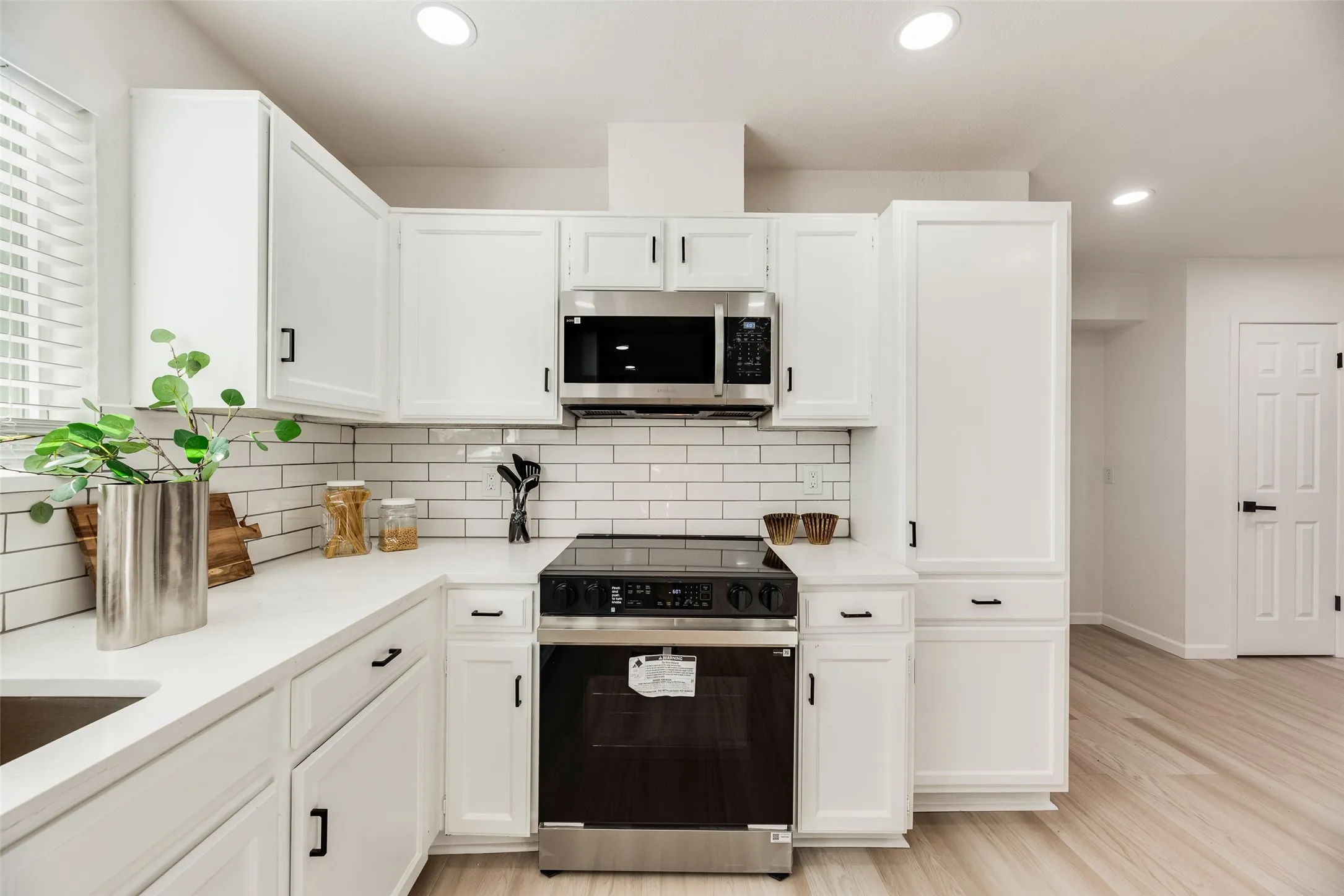 Kitchen featuring crisp white cabinetry, stainless steel appliances, white subway tile backsplash, recessed lighting, and light wood-finish flooring