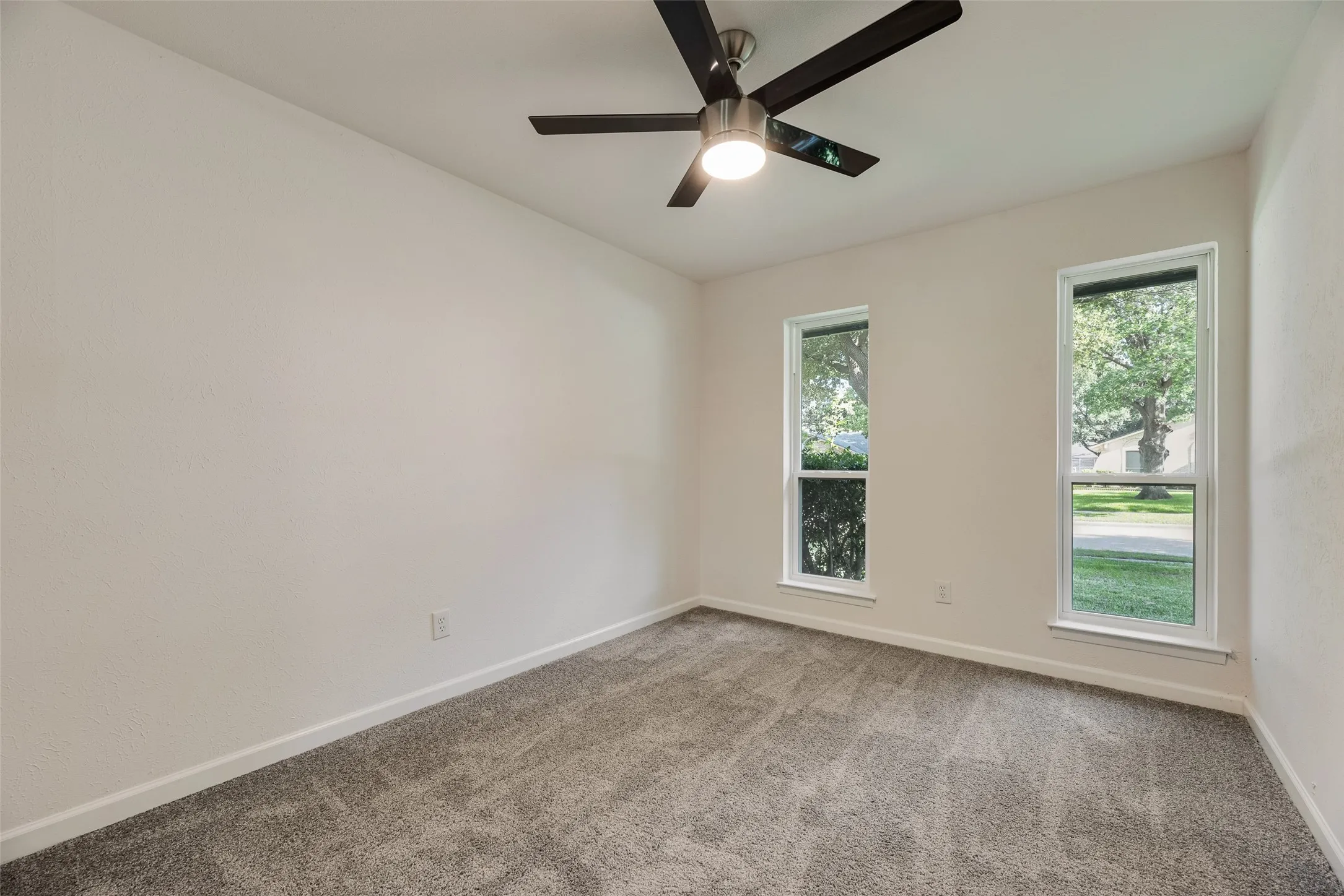 Neutral wall finishes featuring a ceiling fan with integrated lighting, two vertically oriented windows, and gray carpet flooring