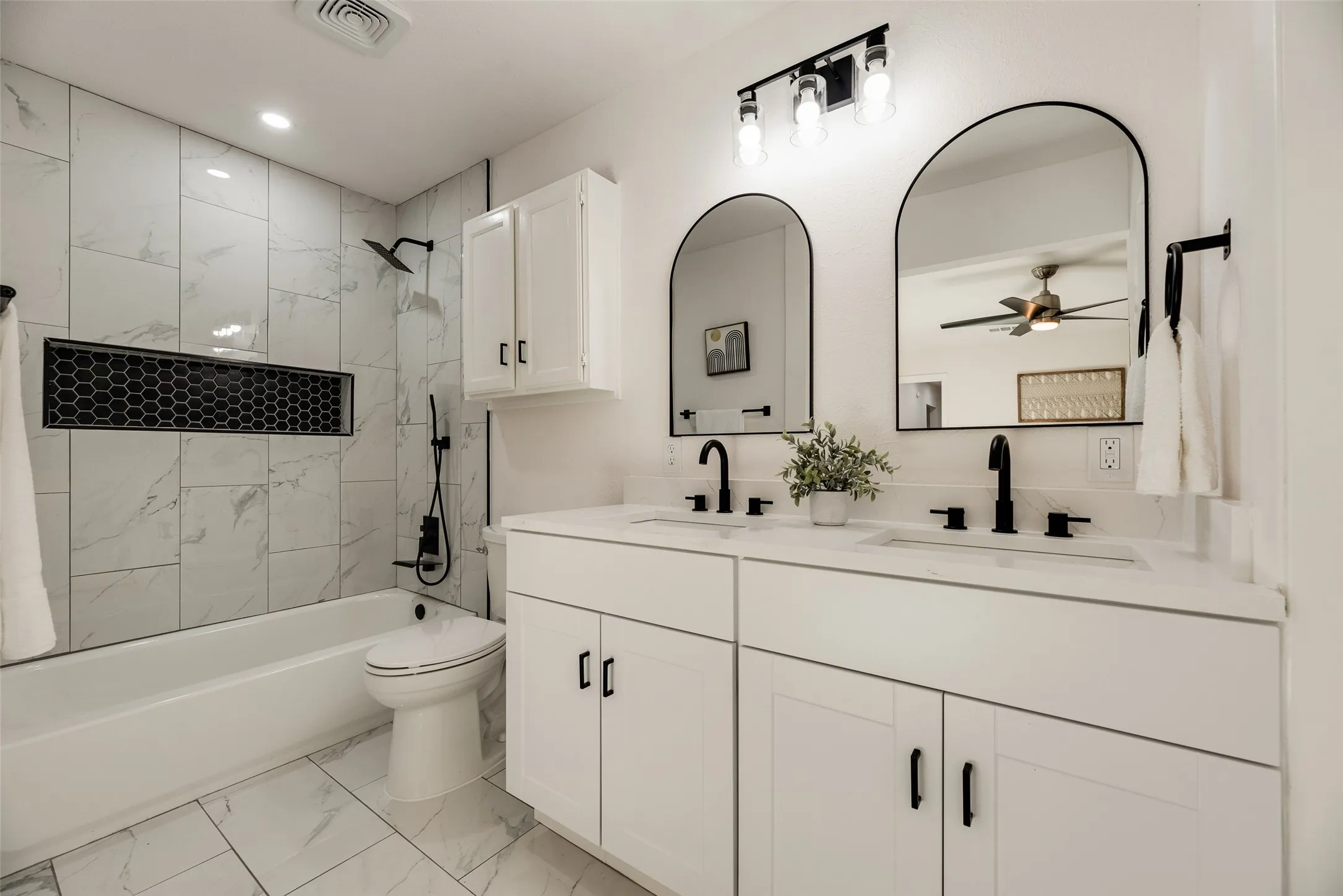 Contemporary bathroom featuring a double vanity with white cabinetry, matte black fixtures, and two arched mirrors