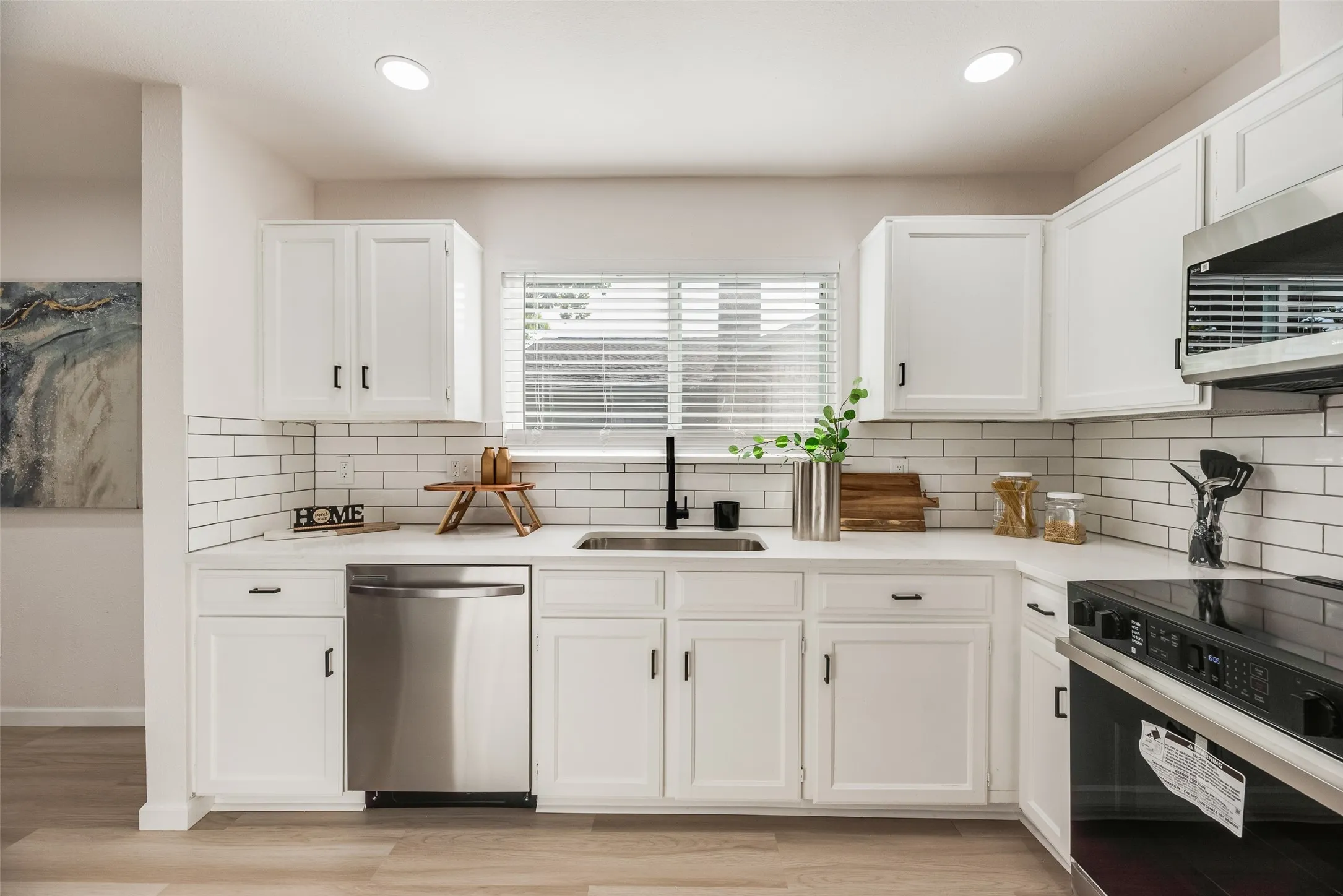 Kitchen featuring white cabinetry, subway tile backsplash, stainless steel dishwasher, and a built-in oven with microwave