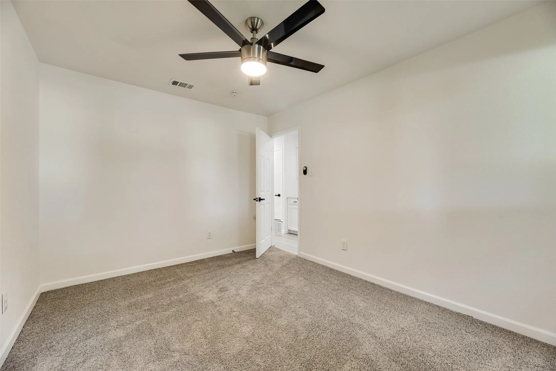 Spacious interior room featuring light gray carpet, white walls, and a ceiling fan with integrated lighting