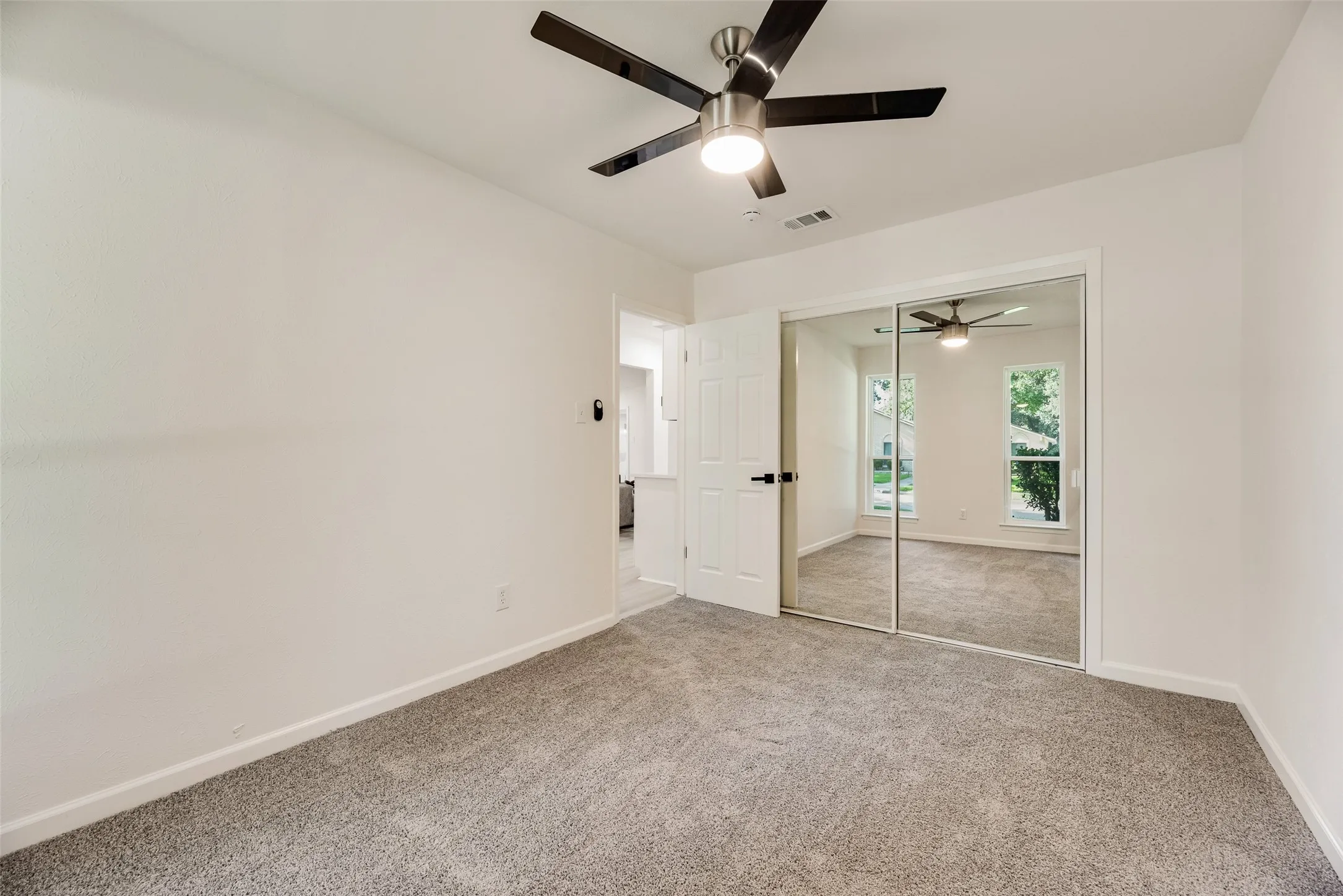 Carpeted room featuring a ceiling fan with integrated lighting, white walls, and a mirrored closet door