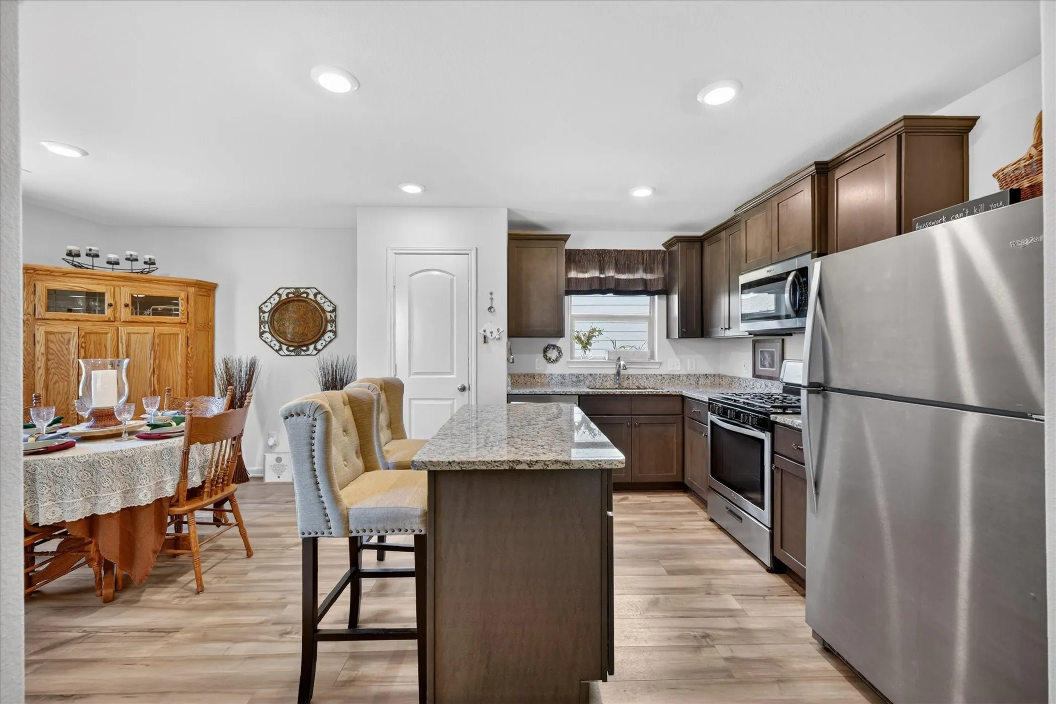 Kitchen featuring granite countertops, wood-finish flooring, recessed lighting, stainless steel appliances, and dark wood cabinetry
