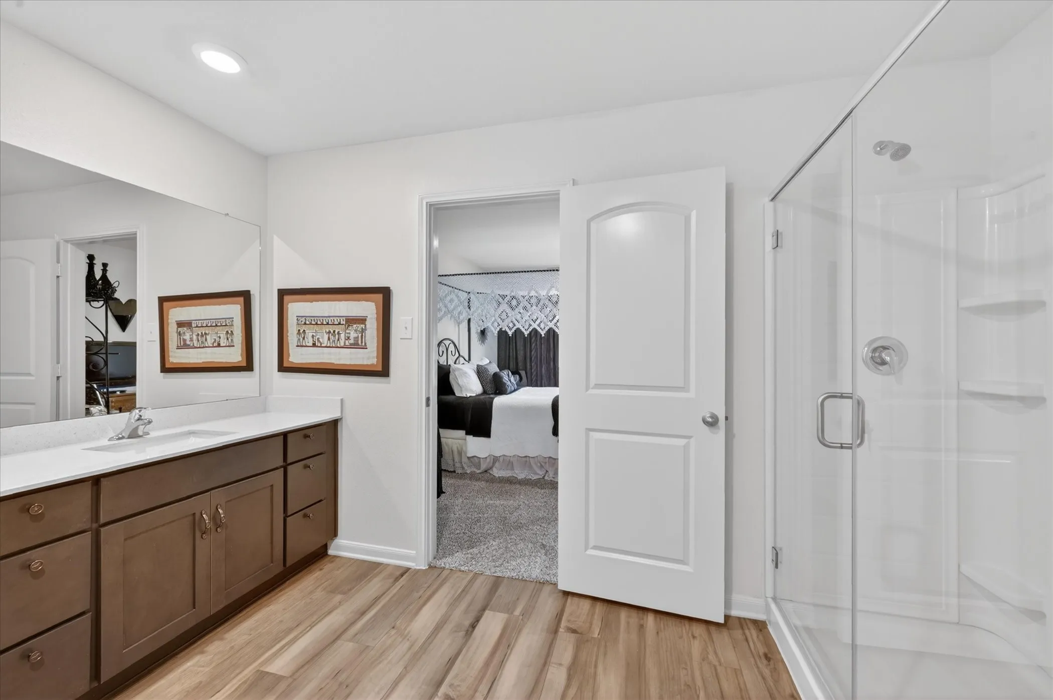 Bathroom featuring wood-finish flooring, a glass-enclosed shower, a double vanity with a white countertop, and recessed lighting