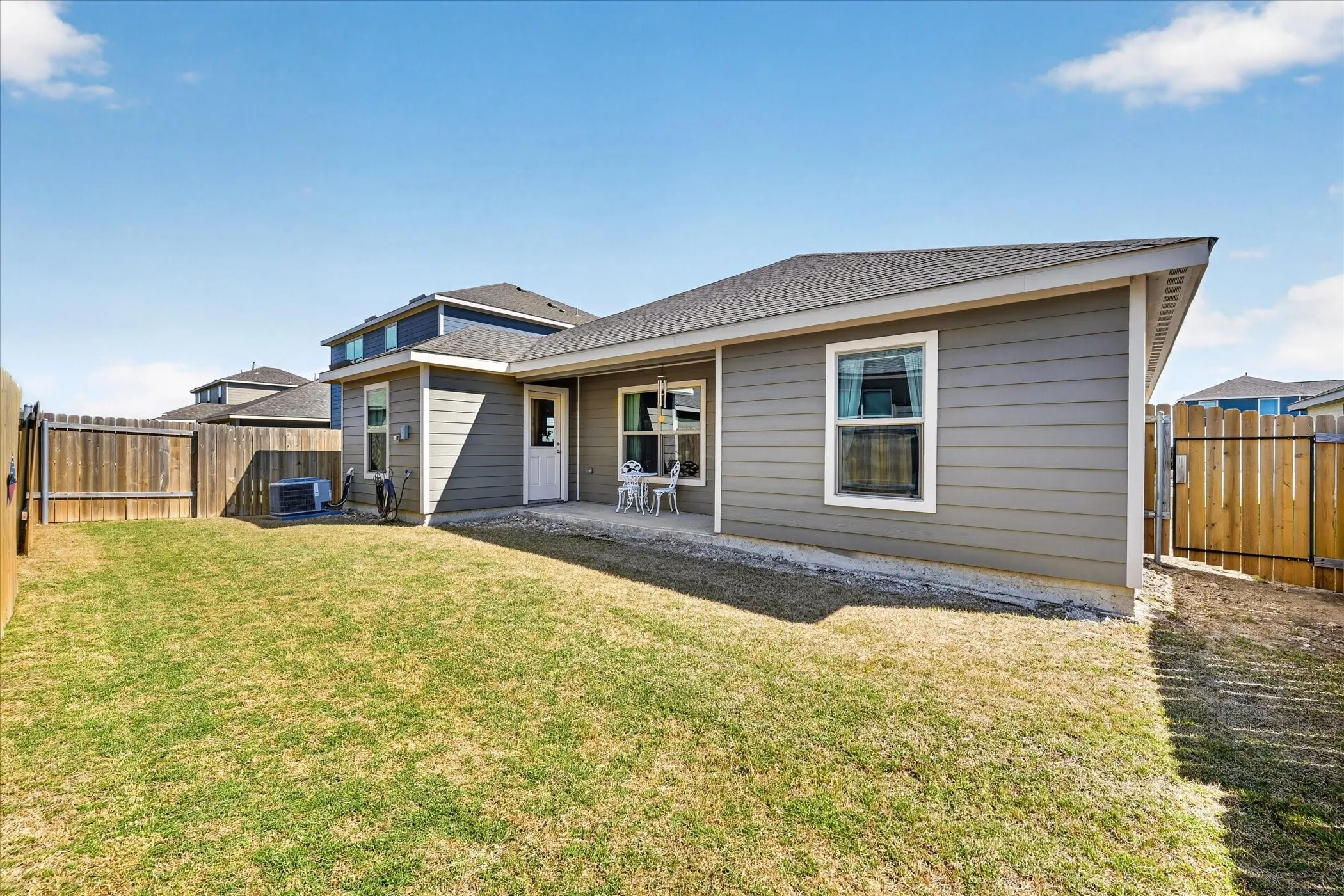 Expansive backyard featuring a concrete patio, wood fencing, and a side gate