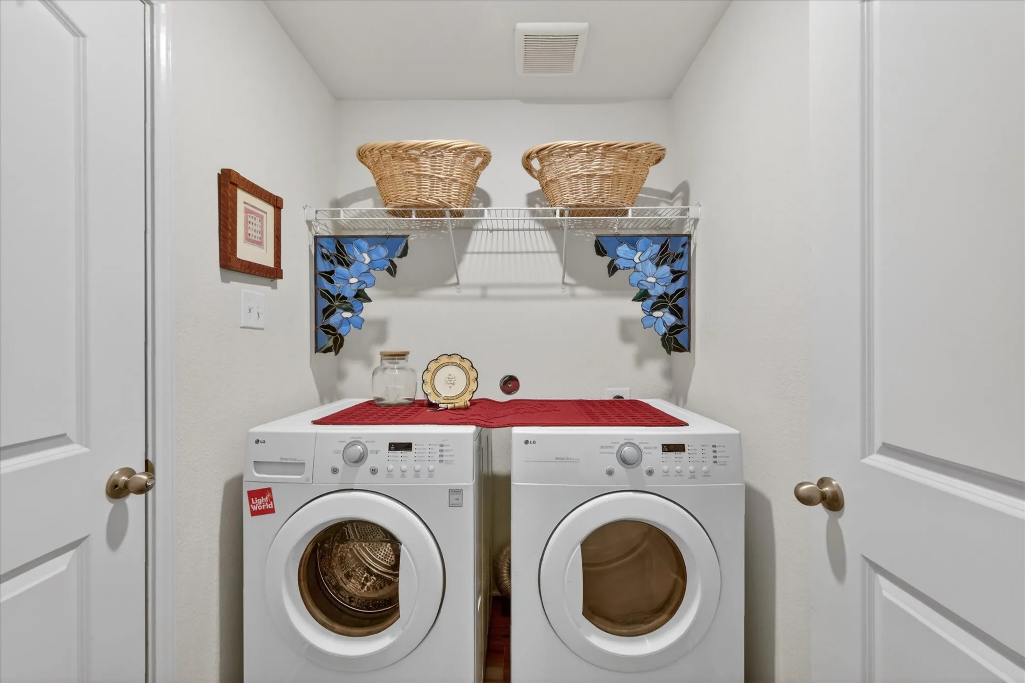 Dedicated laundry area featuring white walls, a white wire shelf with decorative blue floral brackets, and two white panel doors
