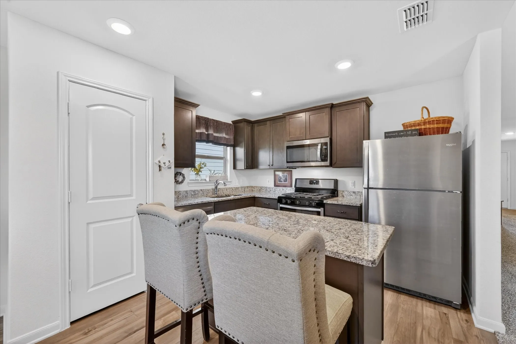Modern kitchen featuring rich wood cabinetry, stainless steel appliances including a gas cooktop and refrigerator, granite countertops, and a spacious island with seating for two