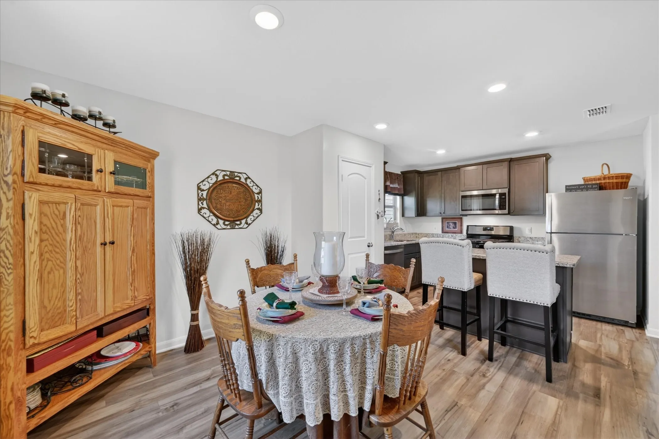 Open-concept kitchen and dining area featuring recessed lighting, wood-finish flooring, a kitchen island with seating, dark wood cabinetry, and stainless steel appliances