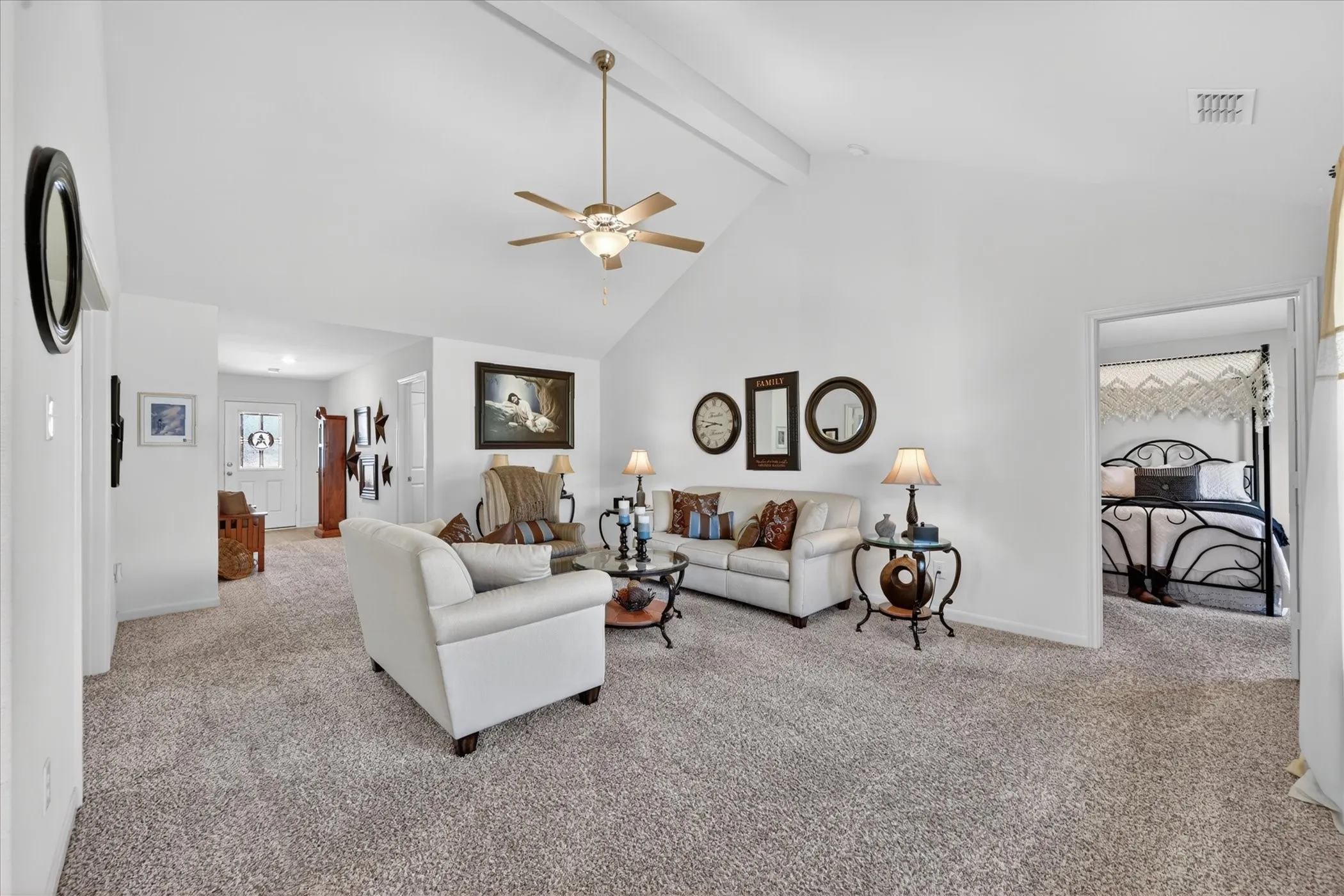 Spacious primary living area featuring vaulted ceilings with ceiling fan, neutral carpet flooring, and abundant natural light from multiple windows