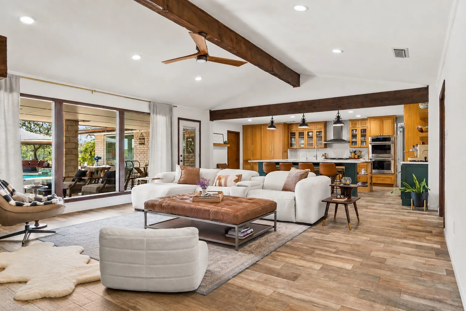 Vaulted ceiling with exposed wood beams, wood-finish flooring, recessed lighting, and a large multi-panel glass door