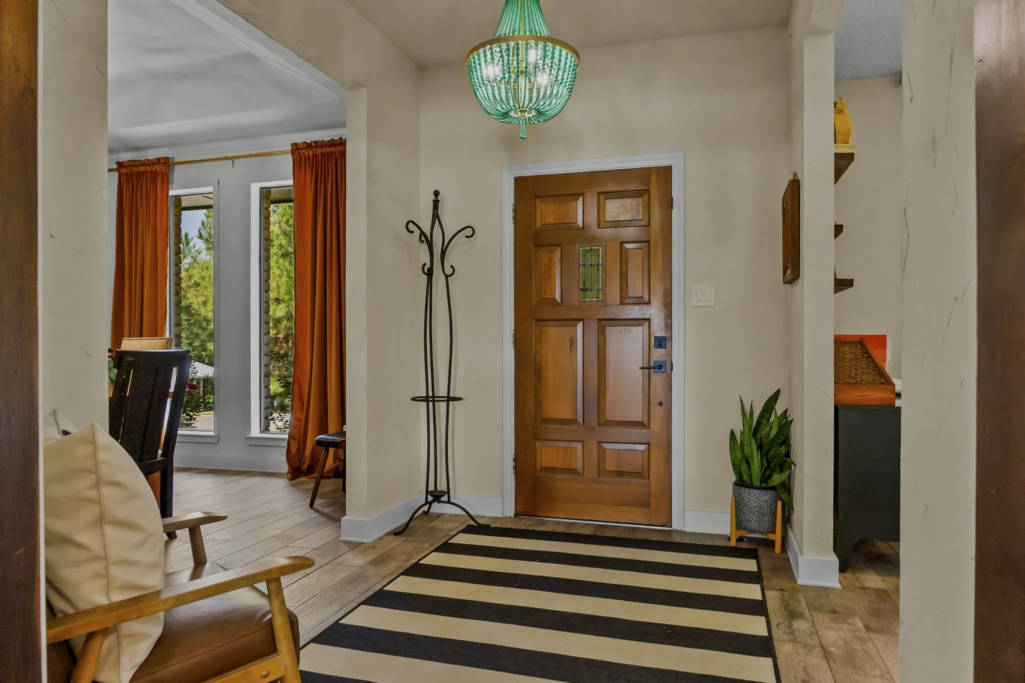 Paneled wood entry door with an inset decorative glass panel, accented by a teal beaded chandelier