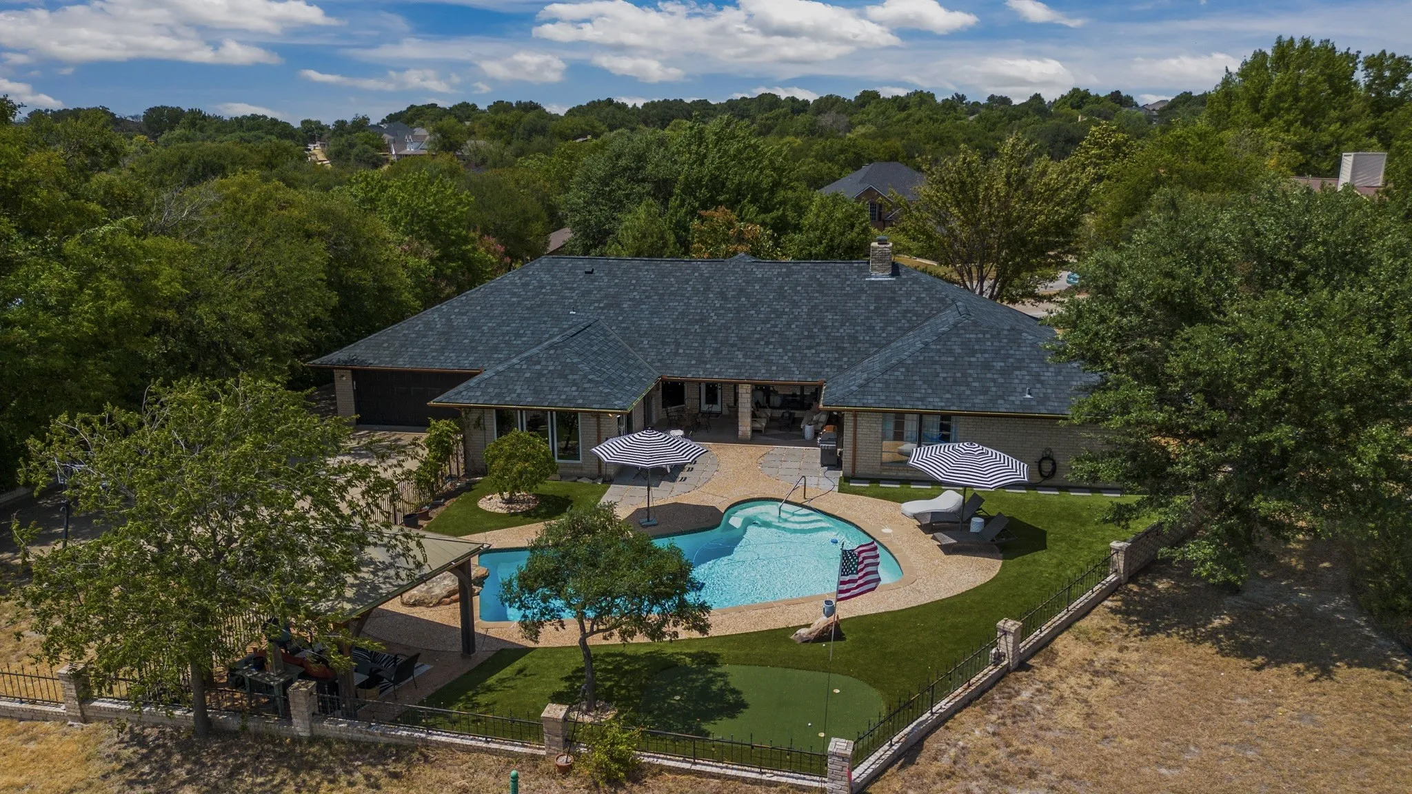 Expansive backyard featuring a custom-shaped swimming pool, paved patio, artificial turf, and a putting green