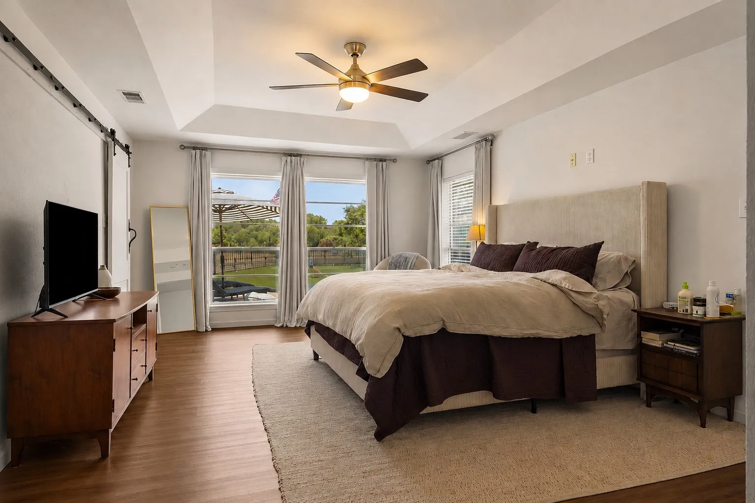 Tray ceiling with a ceiling fan, wood-finish flooring, and multiple windows
