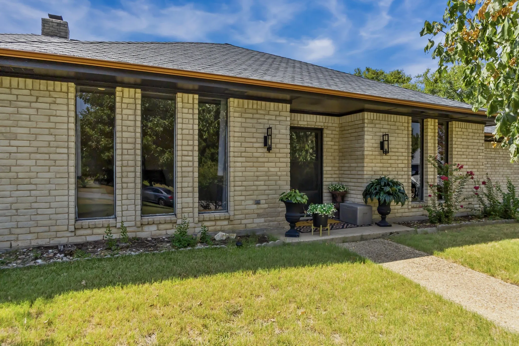 Light-colored brick exterior with dark trim, prominent front entry with sconce lighting, and multiple tall windows