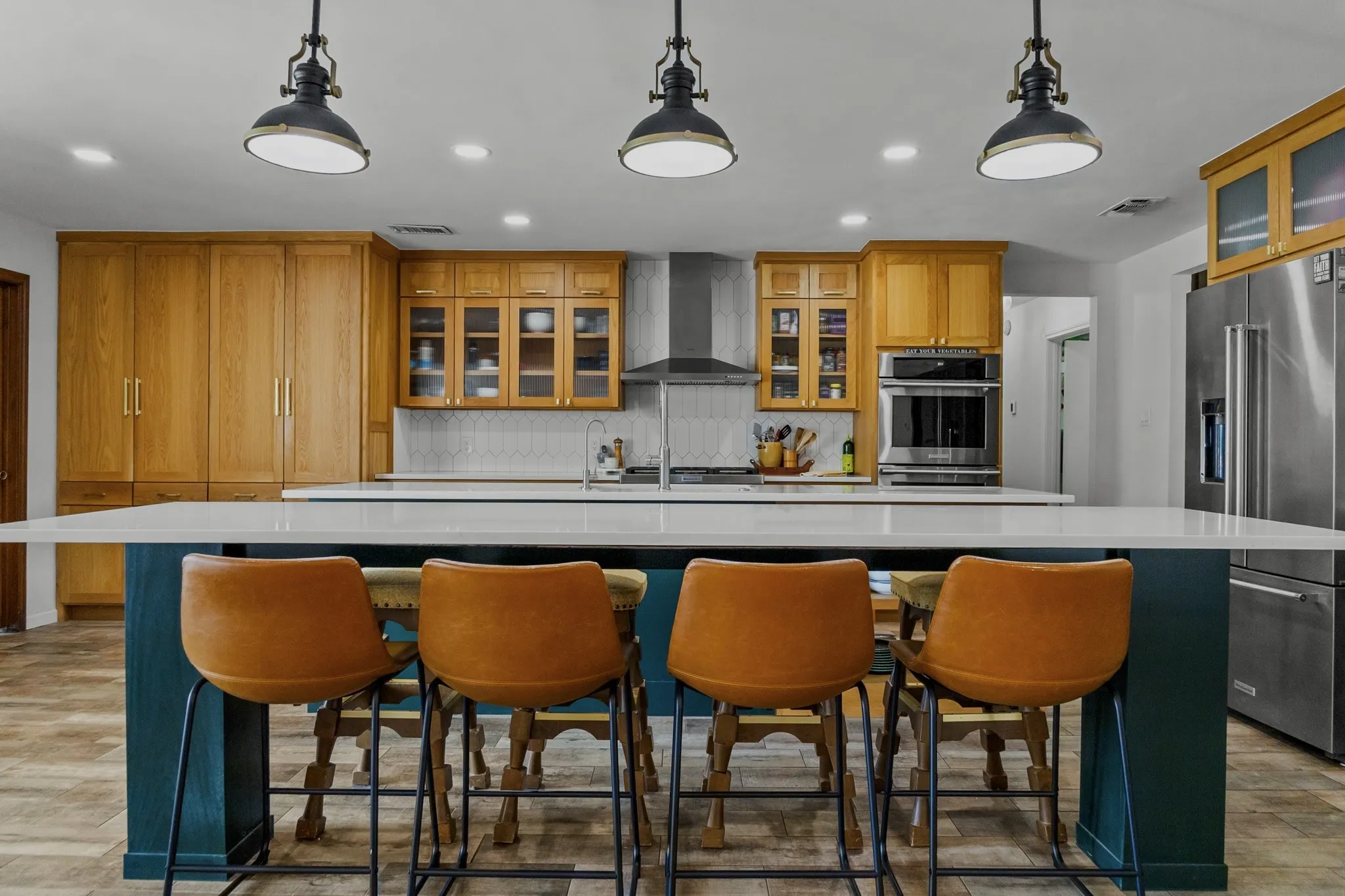 Kitchen featuring a spacious island, built-in stainless steel appliances, wood-finish cabinetry, and a patterned tile backsplash