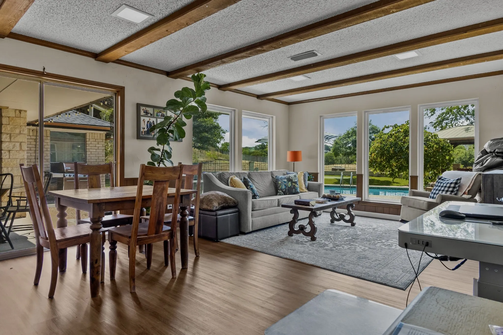 Wood-finish flooring throughout, exposed ceiling beams, multiple large windows, and a sliding glass door