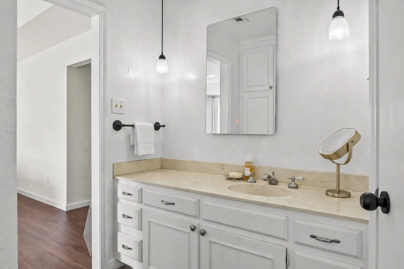 Bathroom vanity with a light-toned countertop, white cabinetry, undermount sink, and wall-mounted mirror