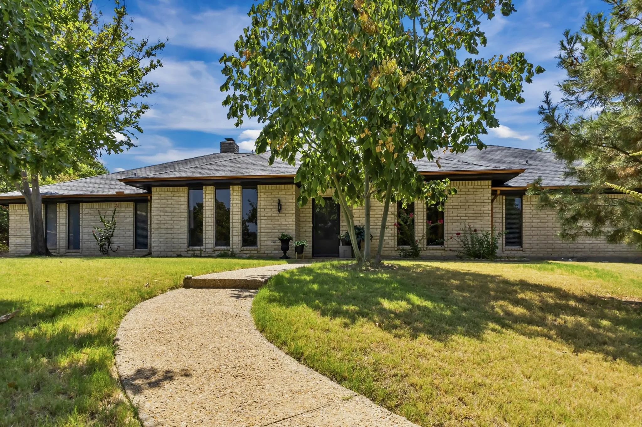 Single-story residence featuring a light brick exterior, dark-framed windows, and a dark shingle roof