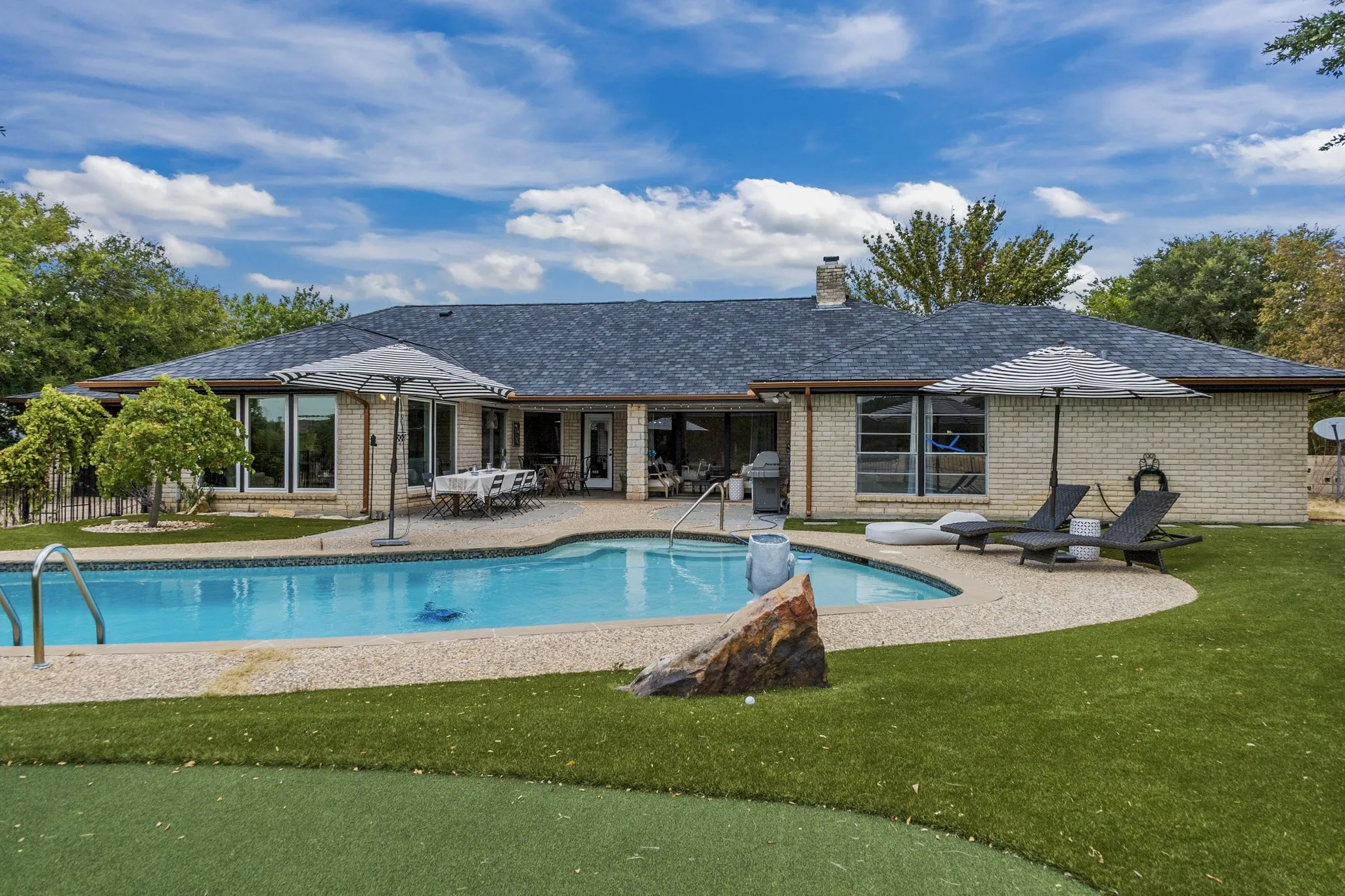 Brick exterior residence featuring a swimming pool, paved patio, and artificial turf lawn