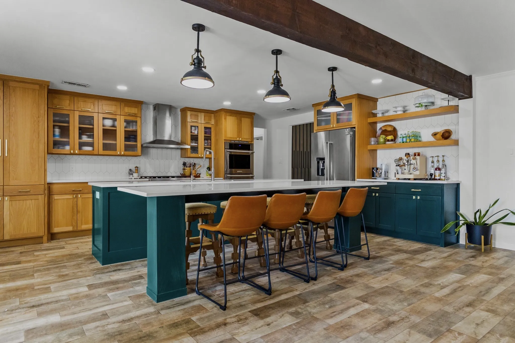 Expansive kitchen featuring a large central island, overhead wood beam, wood-finish flooring, recessed lighting, and a combination of wood and dark cabinetry