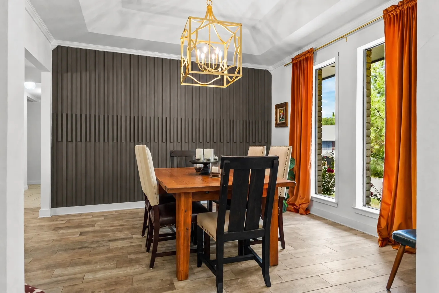 Tray ceiling, wood-finish flooring, two large windows, accent wall with vertical paneling, and a geometric chandelier
