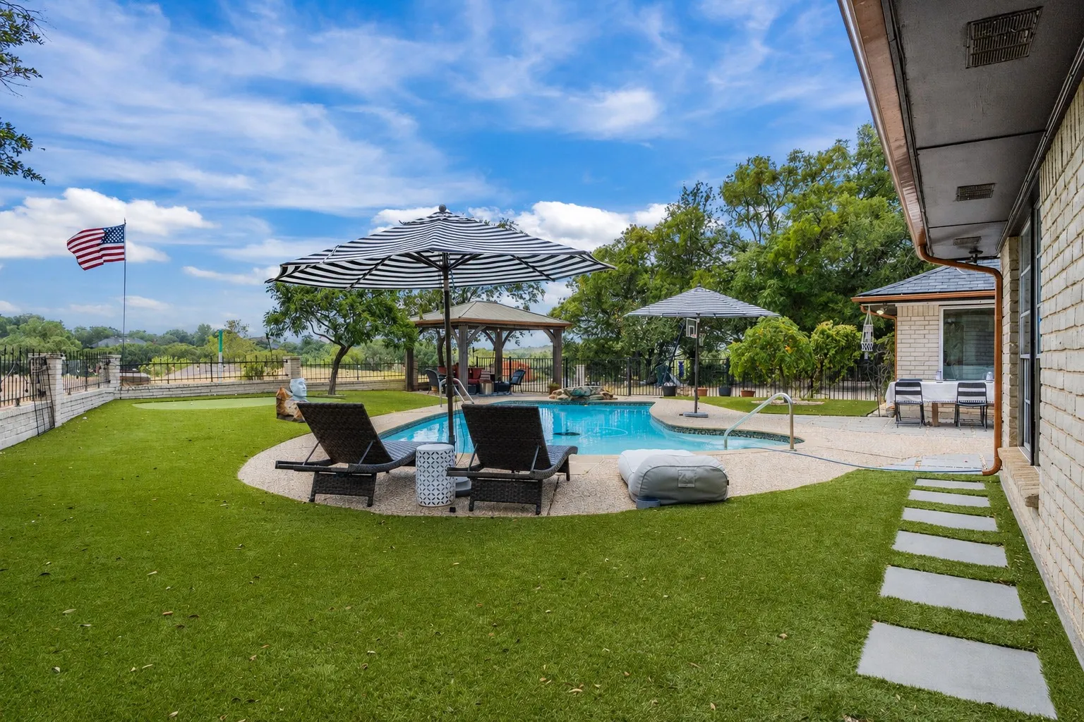 Swimming pool with integrated spa, expansive artificial turf lawn, stone stepping path, brick exterior, and covered patio area