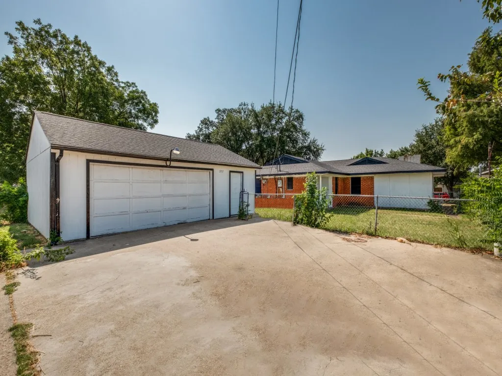 Spacious concrete driveway with two-car garage featuring white paneled door and attached storage room