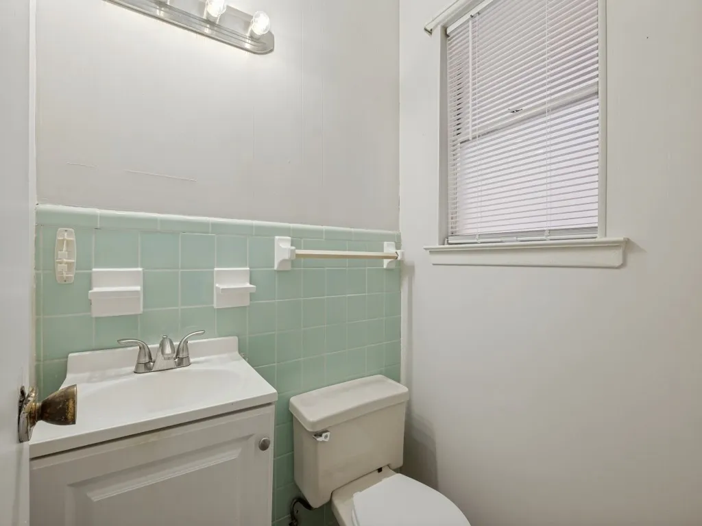 Vintage-inspired bathroom featuring soft green subway tile wainscoting, sink with chrome faucet and fixtures attached to primary bedroom