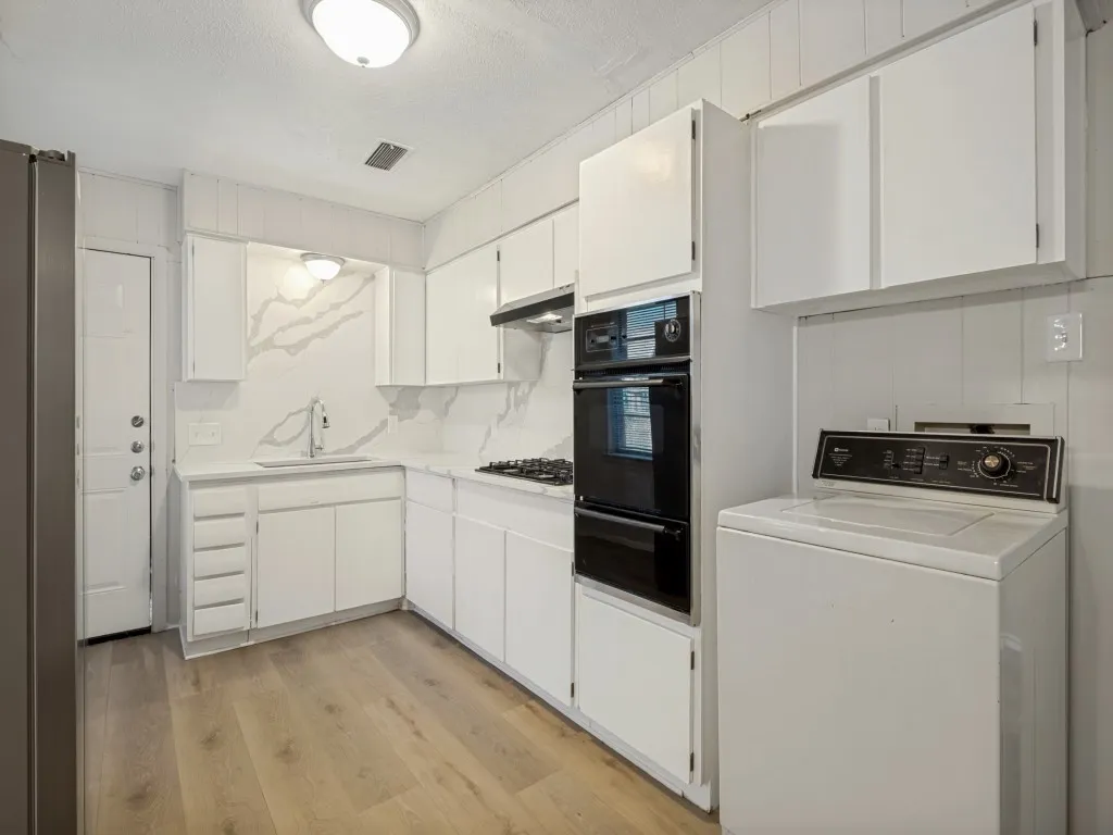 Efficient kitchen layout featuring white cabinetry, stainless steel fridge, dual wall ovens, gas cooktop, vent hood, undermount sink with chrome faucet, and white quartz countertops