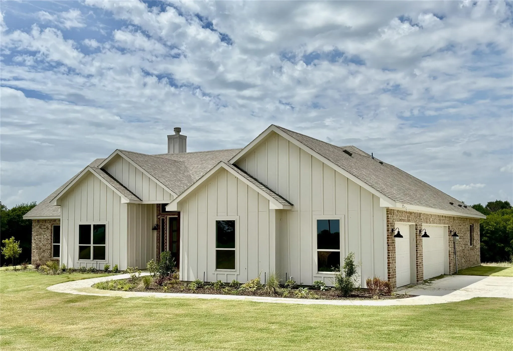 Modern farmhouse exterior featuring board and batten siding, brick accents, a two-car garage, and a curved paved walkway
