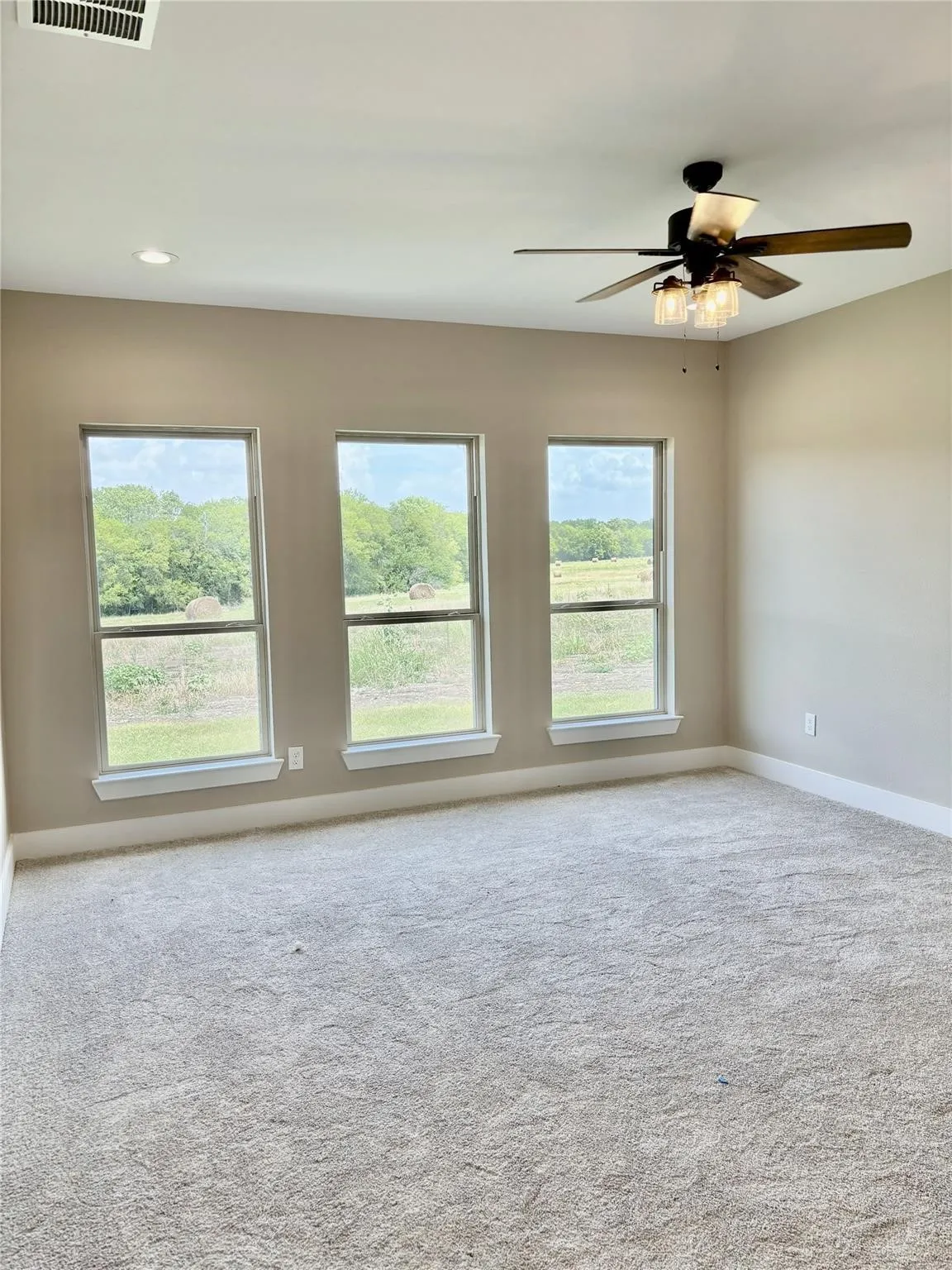 Expansive room featuring light-colored carpeting, a multi-pane window line, and a ceiling fan with integrated lighting