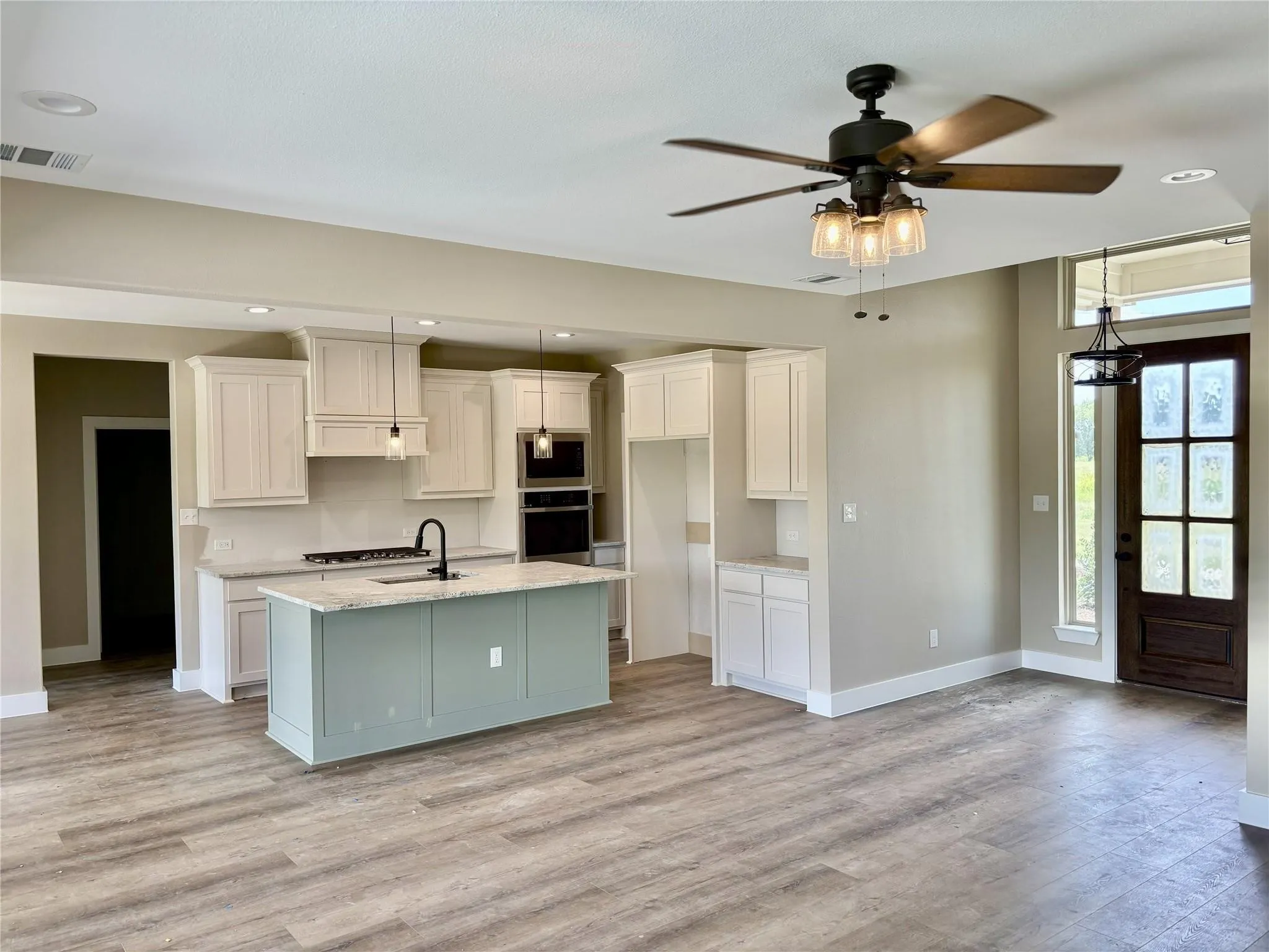 Spacious open-concept kitchen with a light green island, white cabinetry, integrated double ovens, and a gas range