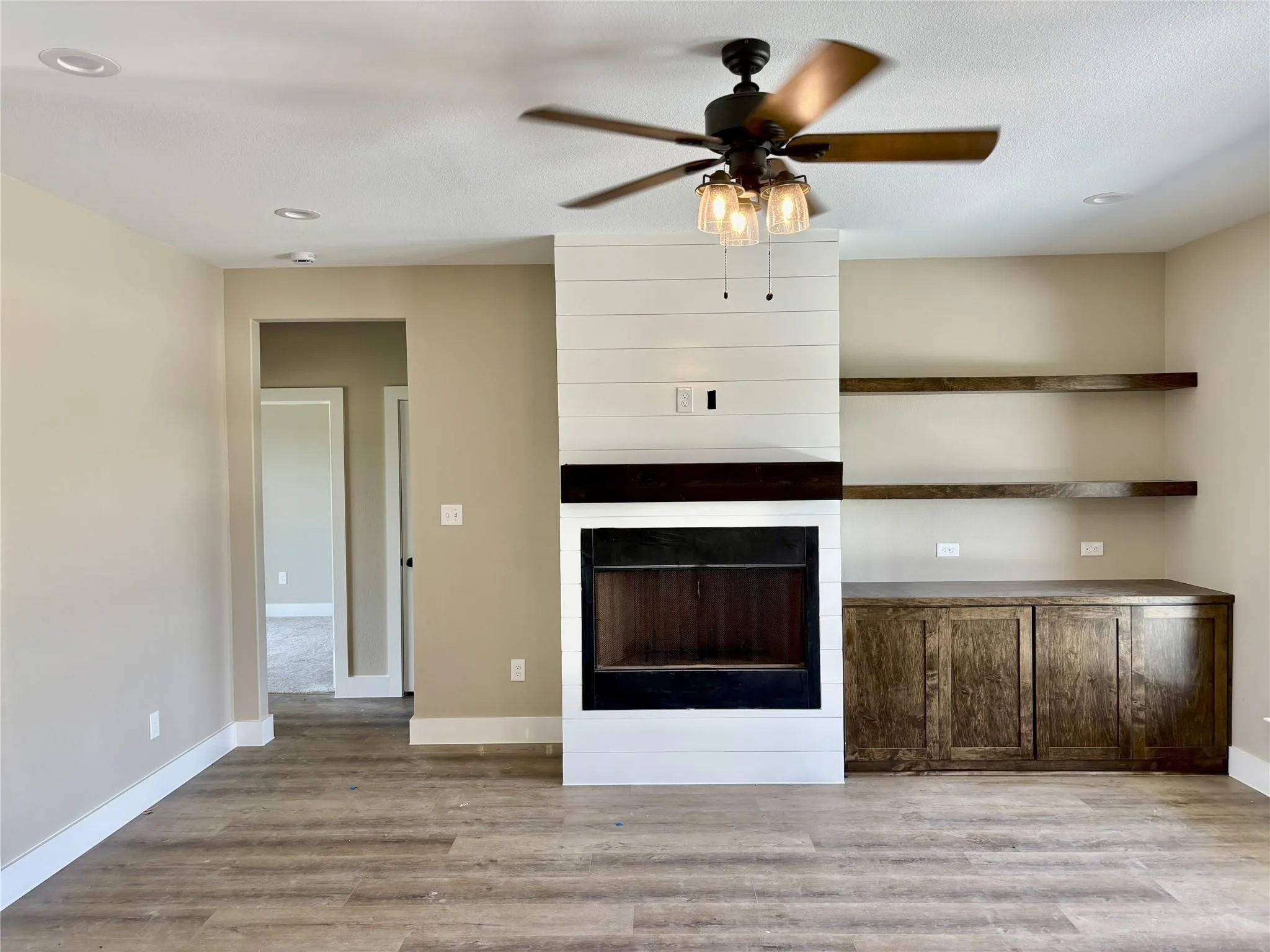 Living area featuring a fireplace with shiplap surround, wood-finish flooring, recessed lighting, and a ceiling fan