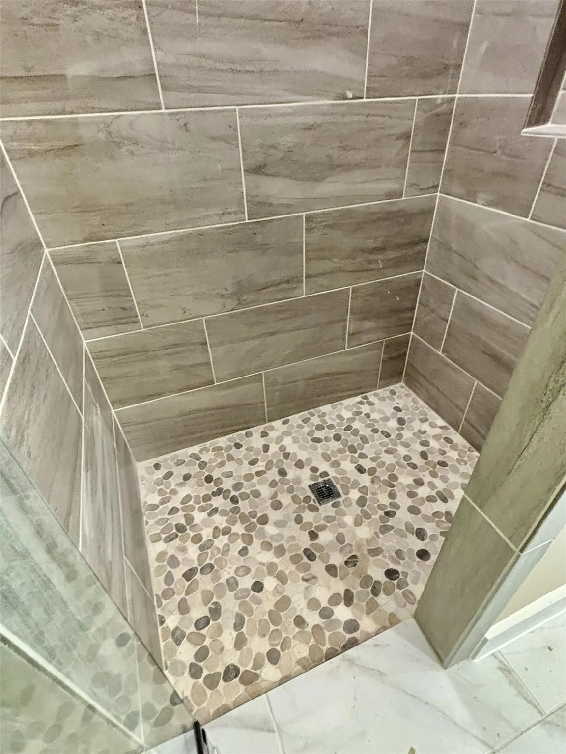 Tiled shower enclosure featuring large-format wall tiles and a pebble stone floor