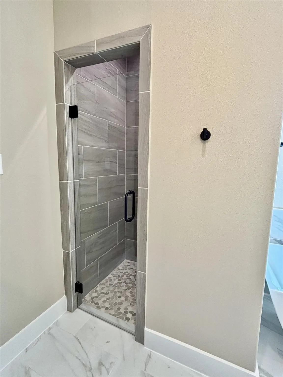 Custom shower enclosure featuring a clear glass door with matte black hardware, gray rectangular wall tiles, and a pebble-style floor