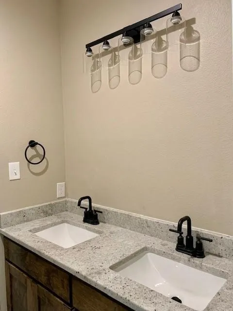 Dual undermount sinks set into a speckled countertop, featuring matte black faucets and a wood-finish vanity with panel doors