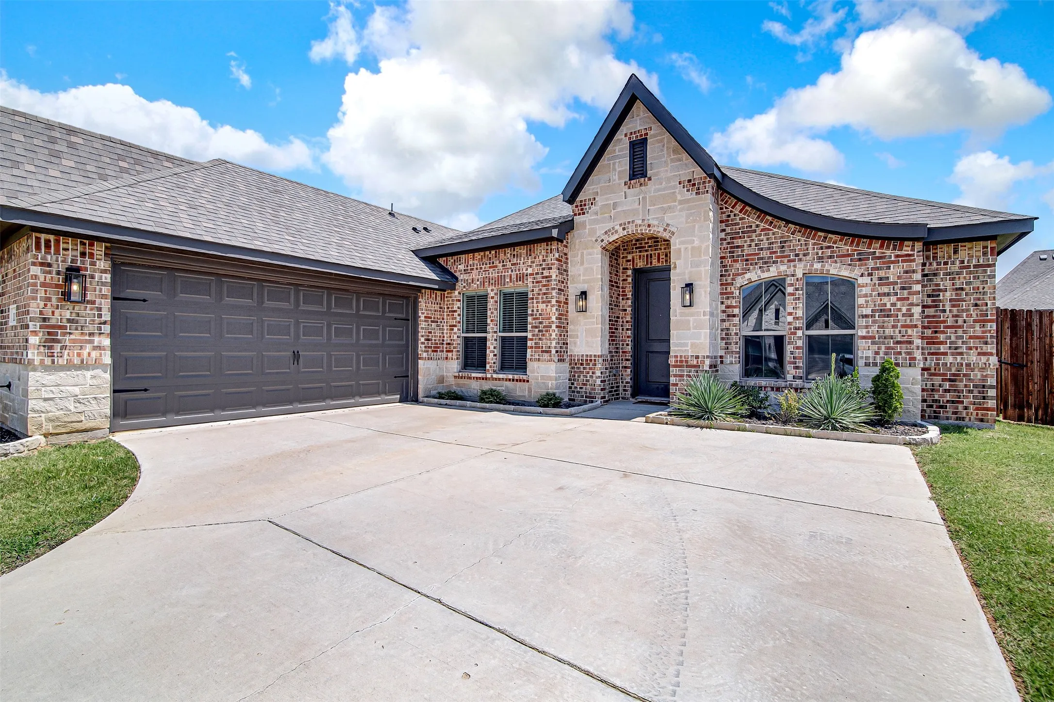 Brick and stone exterior featuring an arched entry, a two-car garage, and a concrete driveway