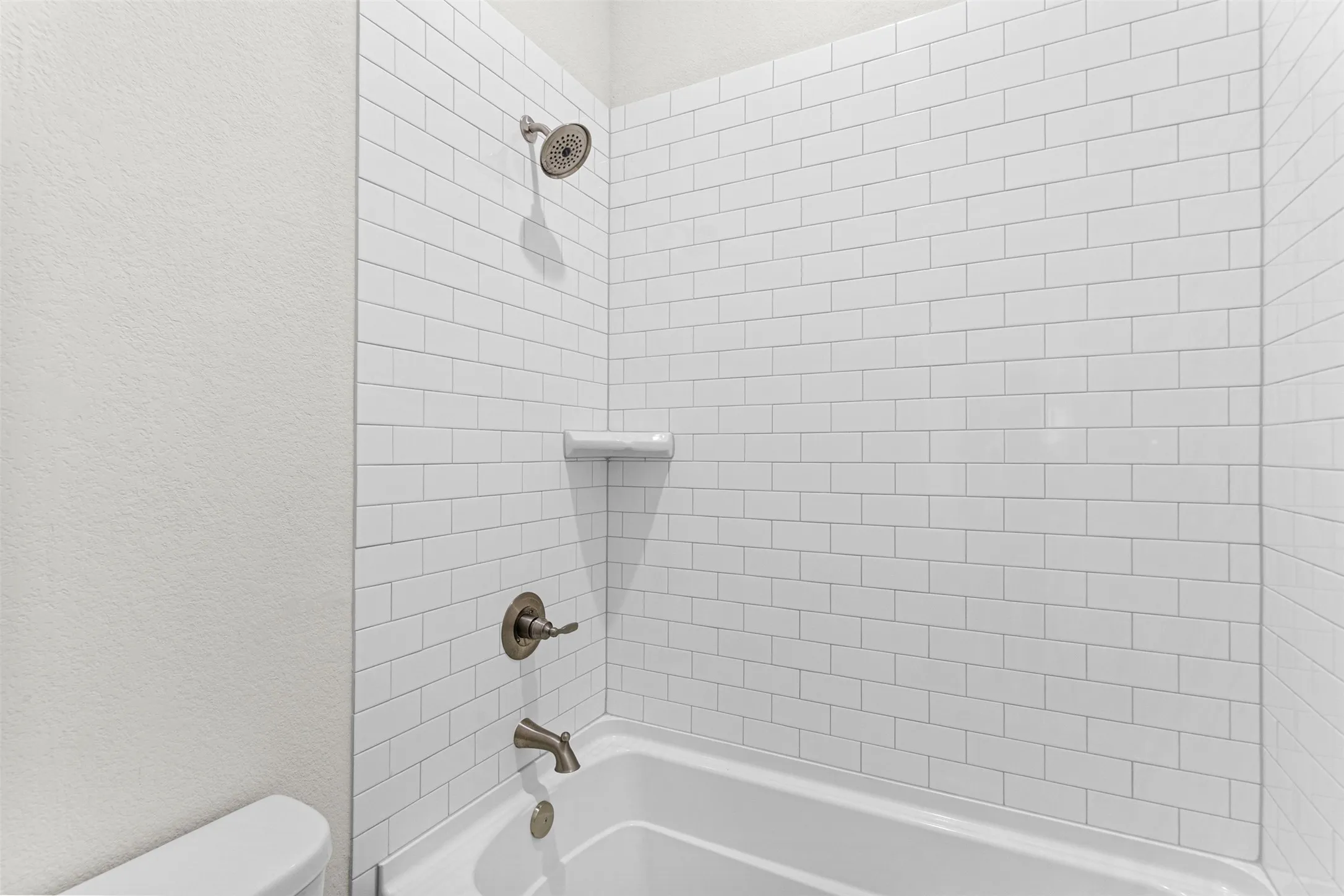 Clean, updated bathroom featuring white subway tile surround, polished chrome fixtures, and a classic white porcelain tub with integrated shower