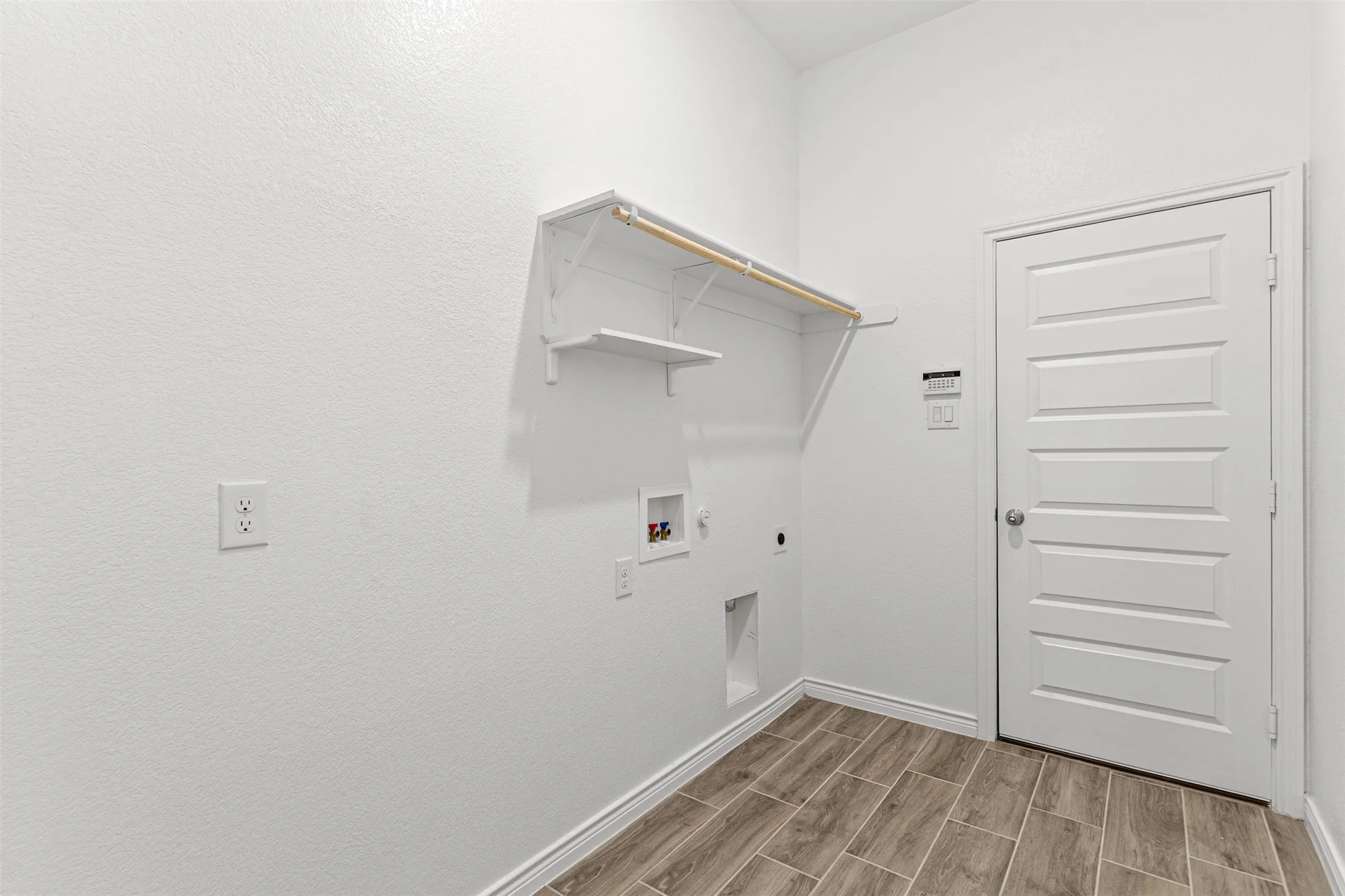 Dedicated laundry room featuring wall-mounted shelving, built-in cabinetry with upper storage, wood-finish flooring, and a white six-panel entry door