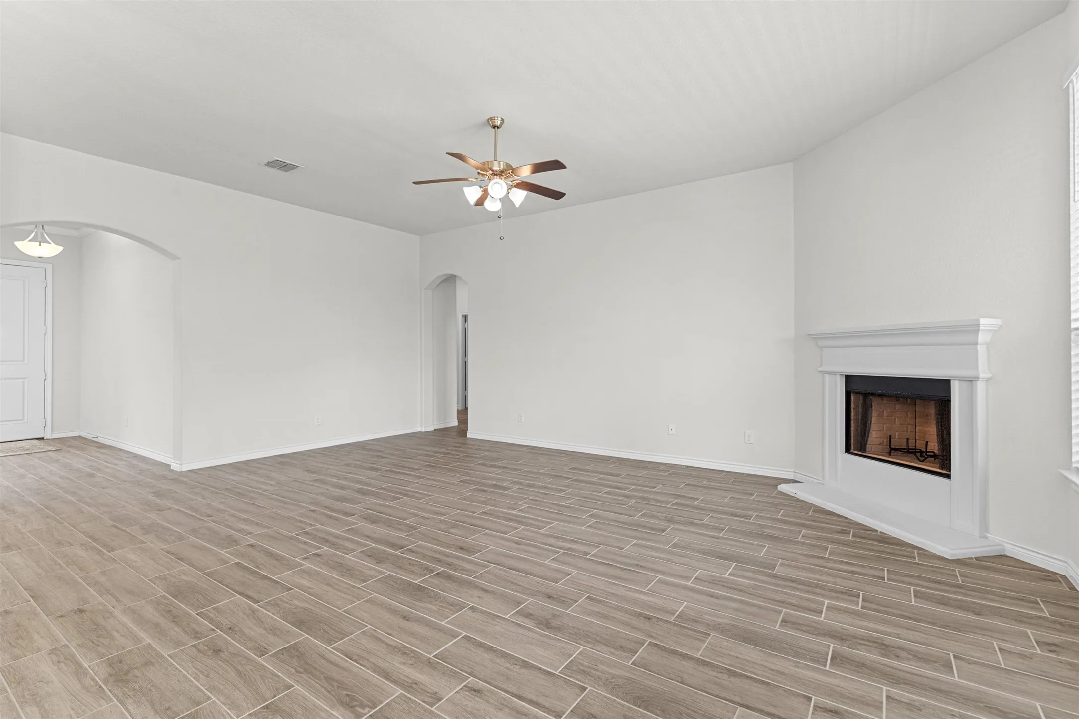 Spacious living area featuring wood-look tile flooring, a fireplace with a classic mantel, and a ceiling fan with integrated lighting