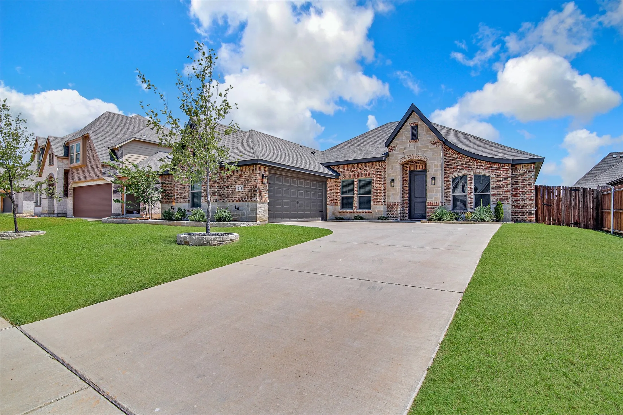 Brick and stone facade residence featuring a dark gray front door, concrete driveway, and attached two-car garage