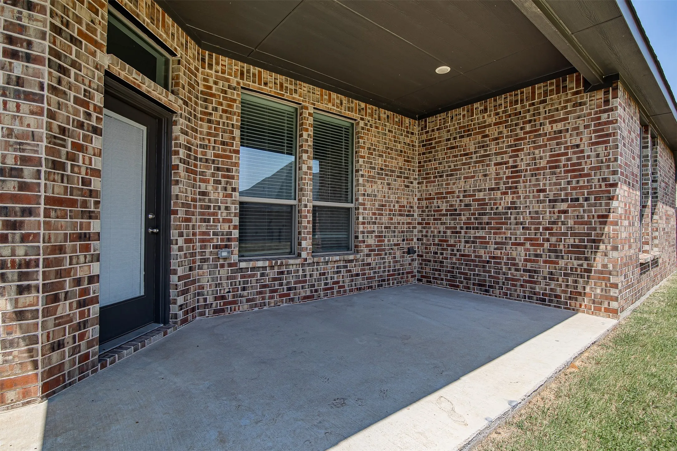 Covered patio featuring durable concrete flooring, brick exterior walls, and large double-hung windows with dark frames