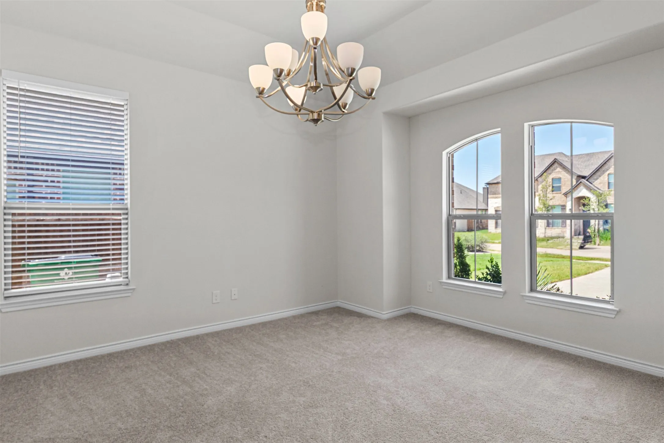 Carpeted room featuring a ceiling-mounted chandelier, arched windows, and a rectangular window with blinds