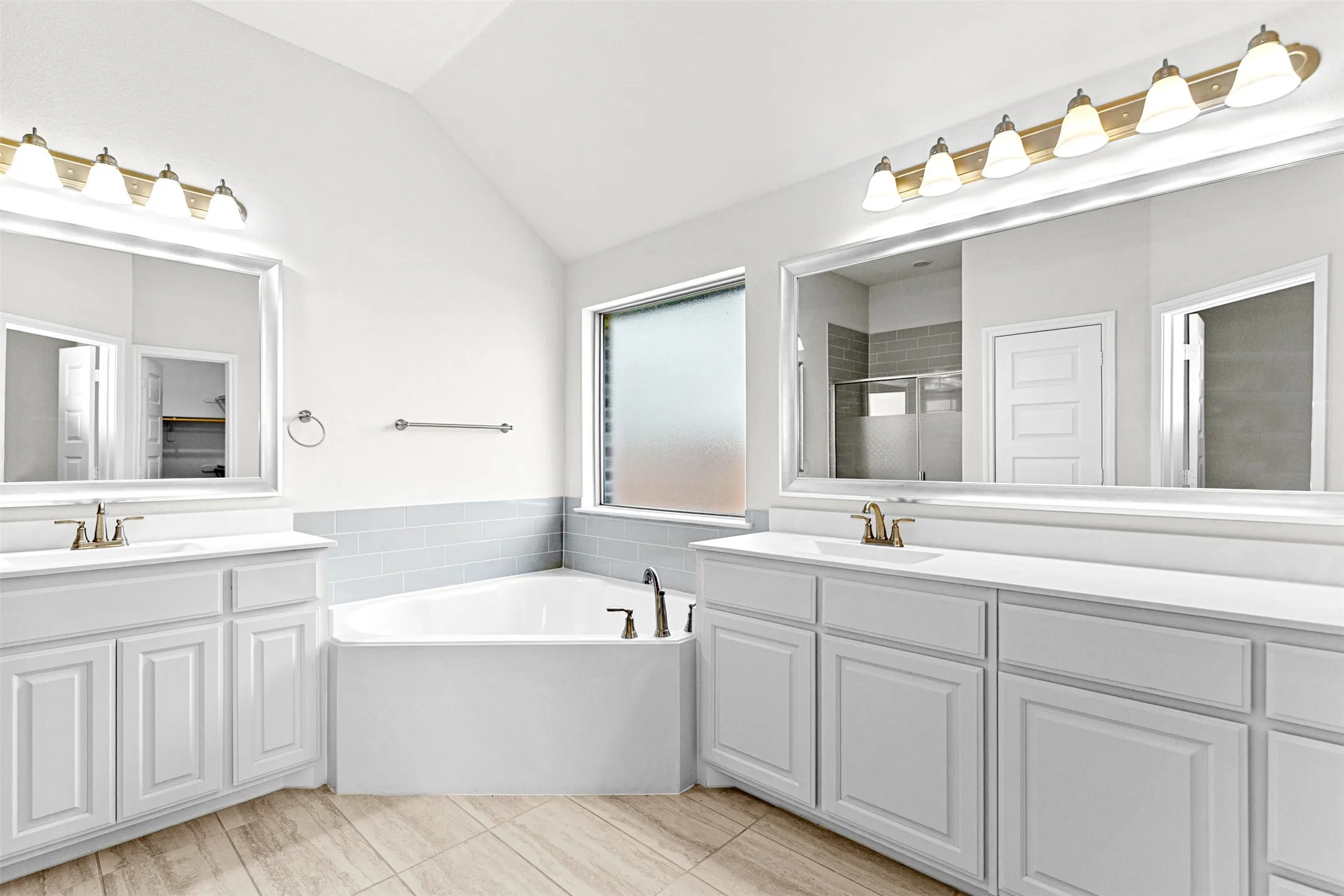 Bathroom featuring a corner soaking tub, dual vanities with white cabinetry, and wood-finish tile flooring