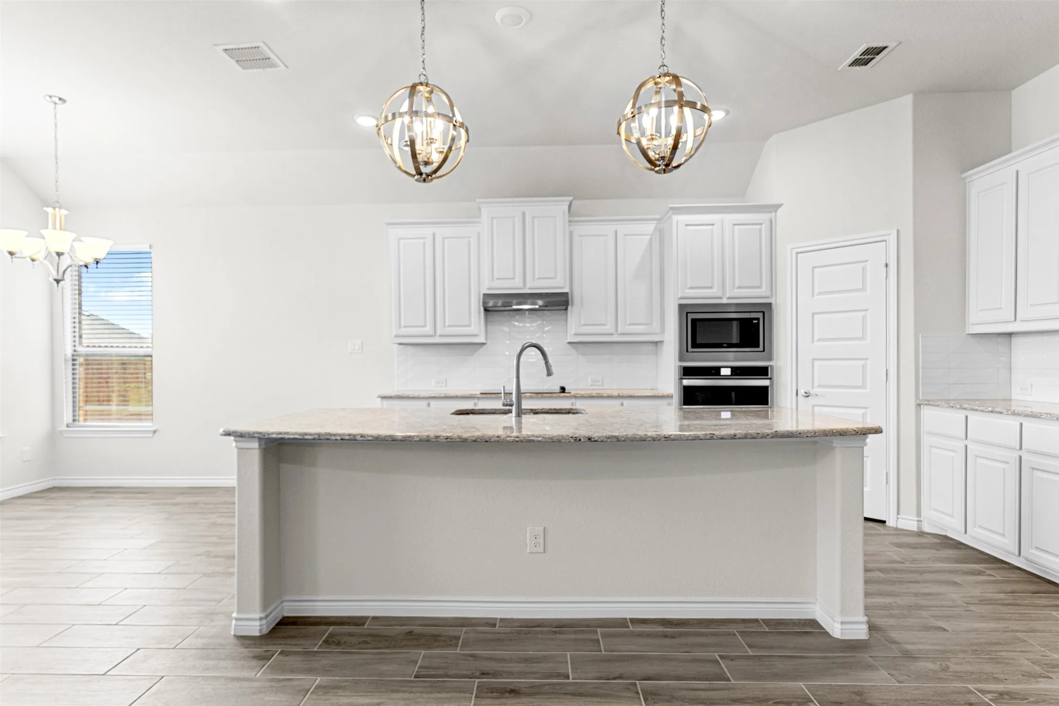 Kitchen island with a built-in sink, stainless steel appliances, white cabinetry, and granite​​‌​​​​‌​​‌‌​‌‌​​​‌‌​‌​‌​‌​​​‌​​ countertops