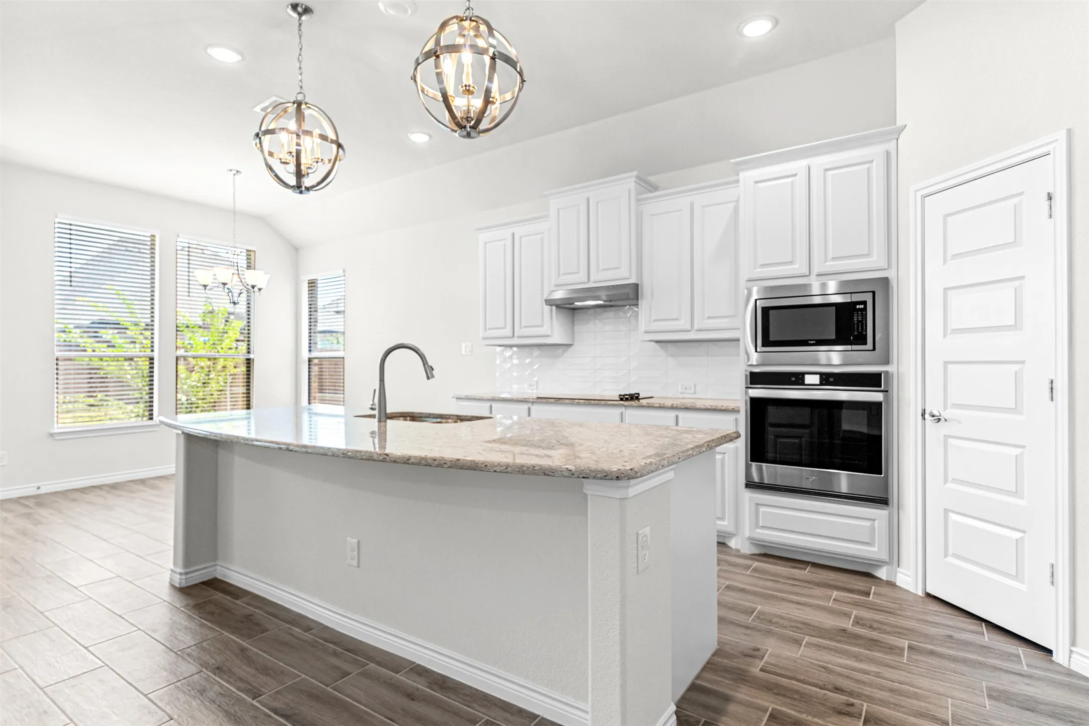 Kitchen featuring a large island with a sink and a gooseneck faucet, light-toned countertops, white cabinetry, and stainless steel appliances including a built-in microwave and oven