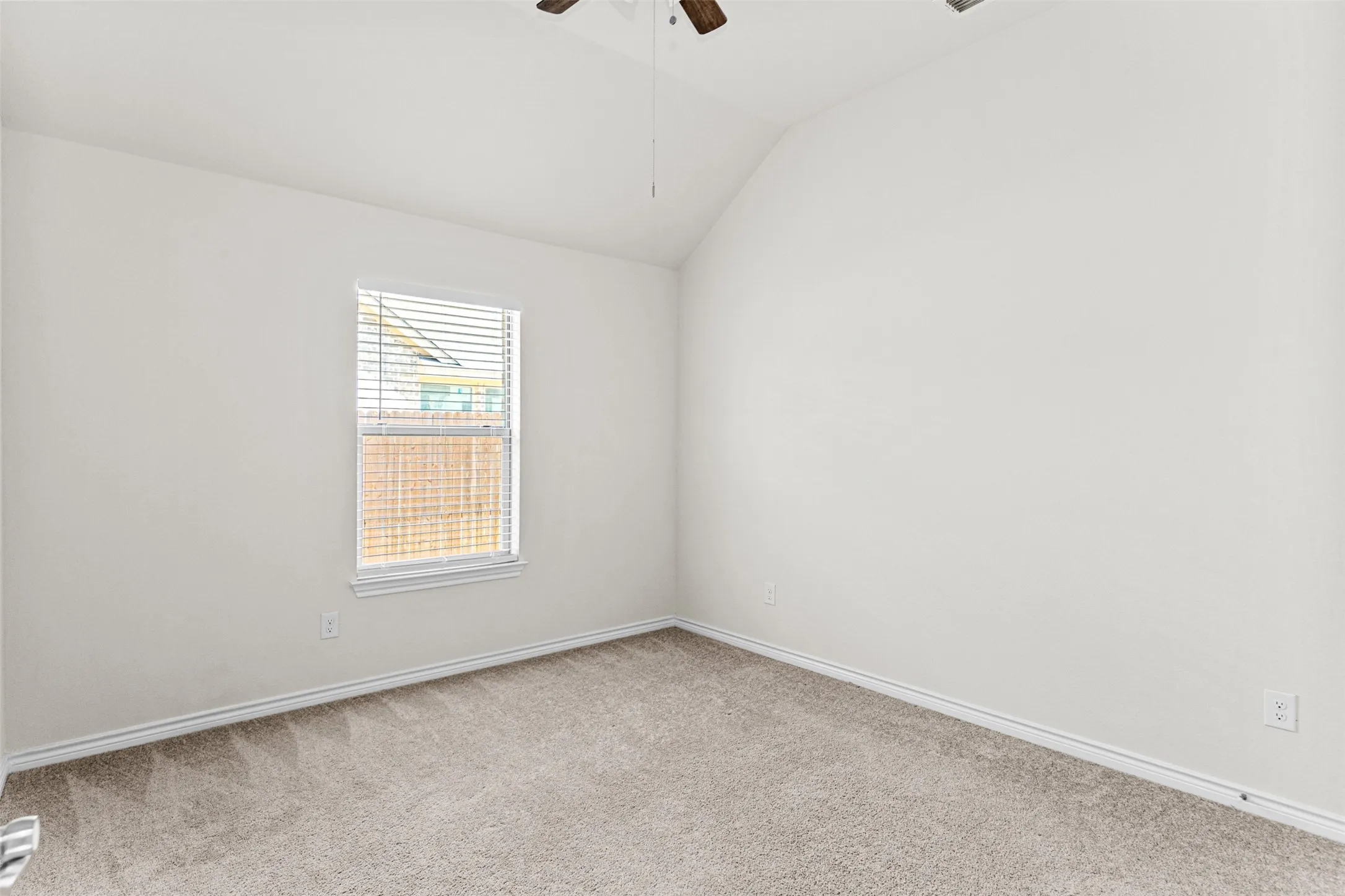Bright bedroom featuring neutral carpeting, clean white walls, and a large window with horizontal blinds providing natural light