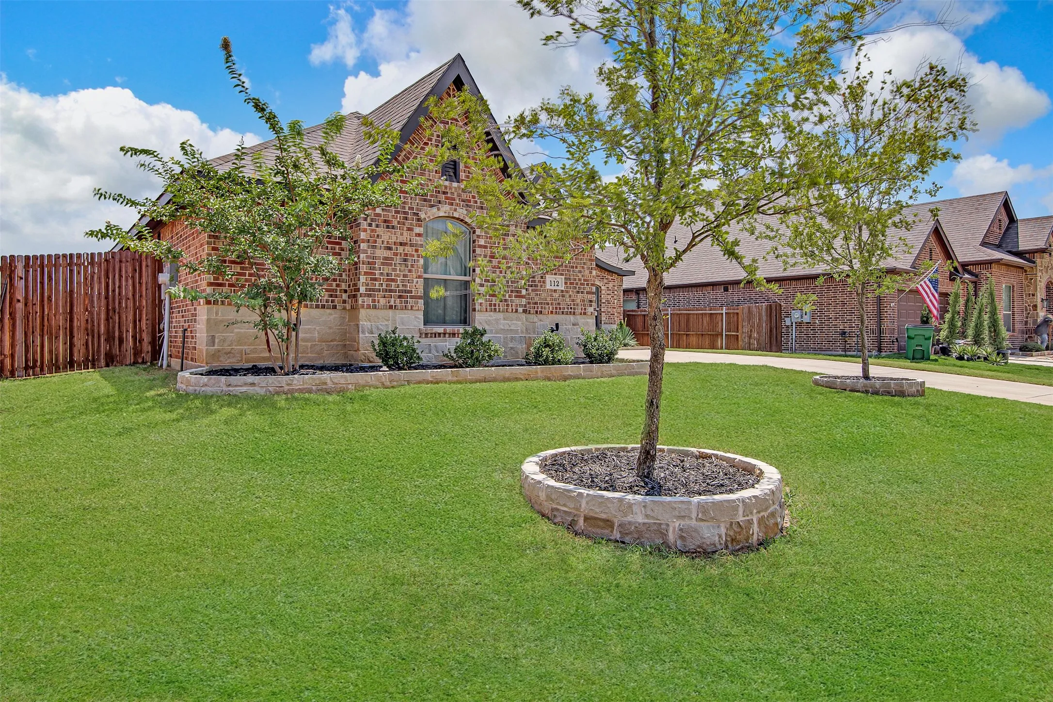 Brick and stone exterior featuring an arched window, a gabled roofline, and foundation planting beds