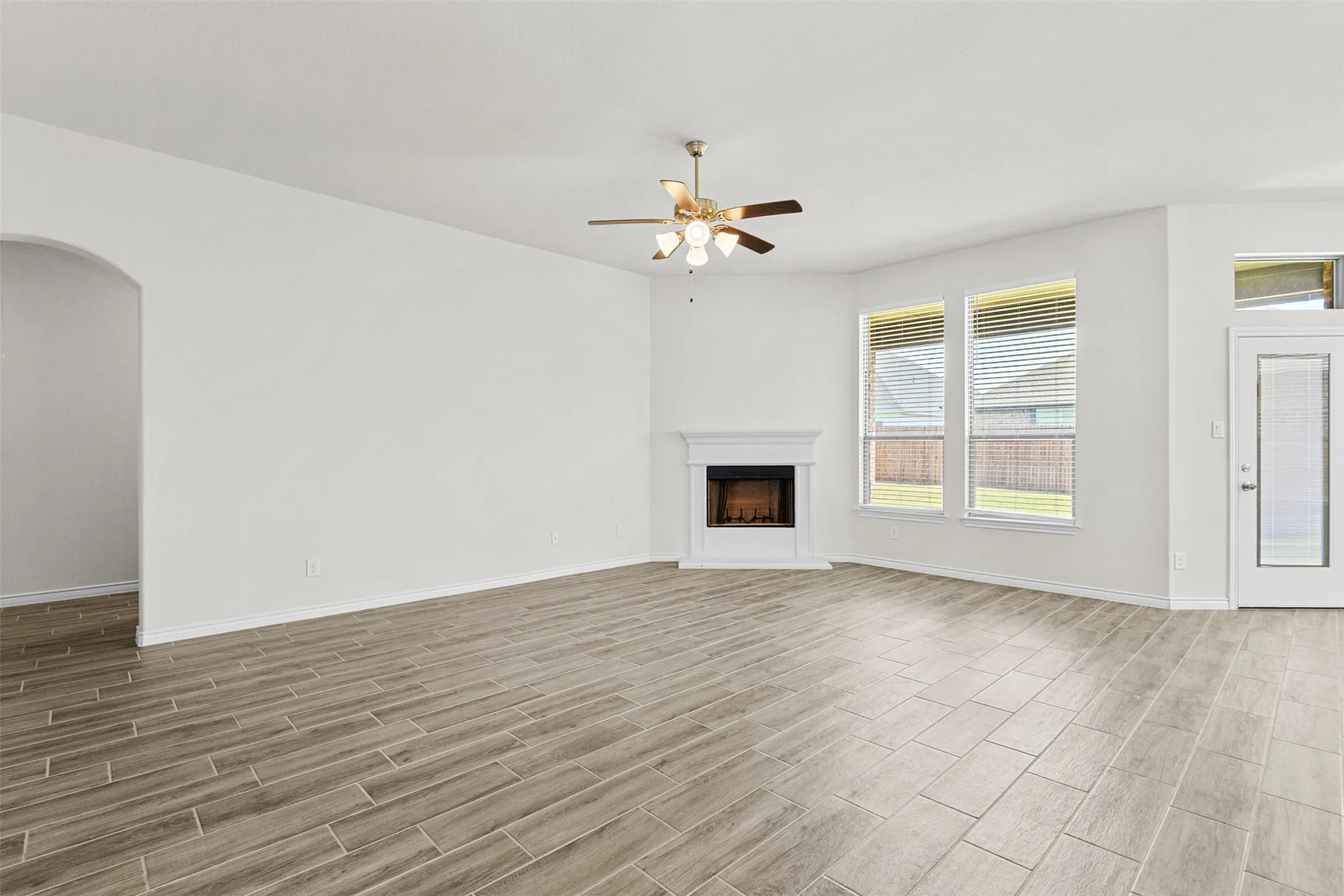 Spacious living area featuring wood-finish tile flooring, a corner fireplace with a white mantel, and a ceiling fan