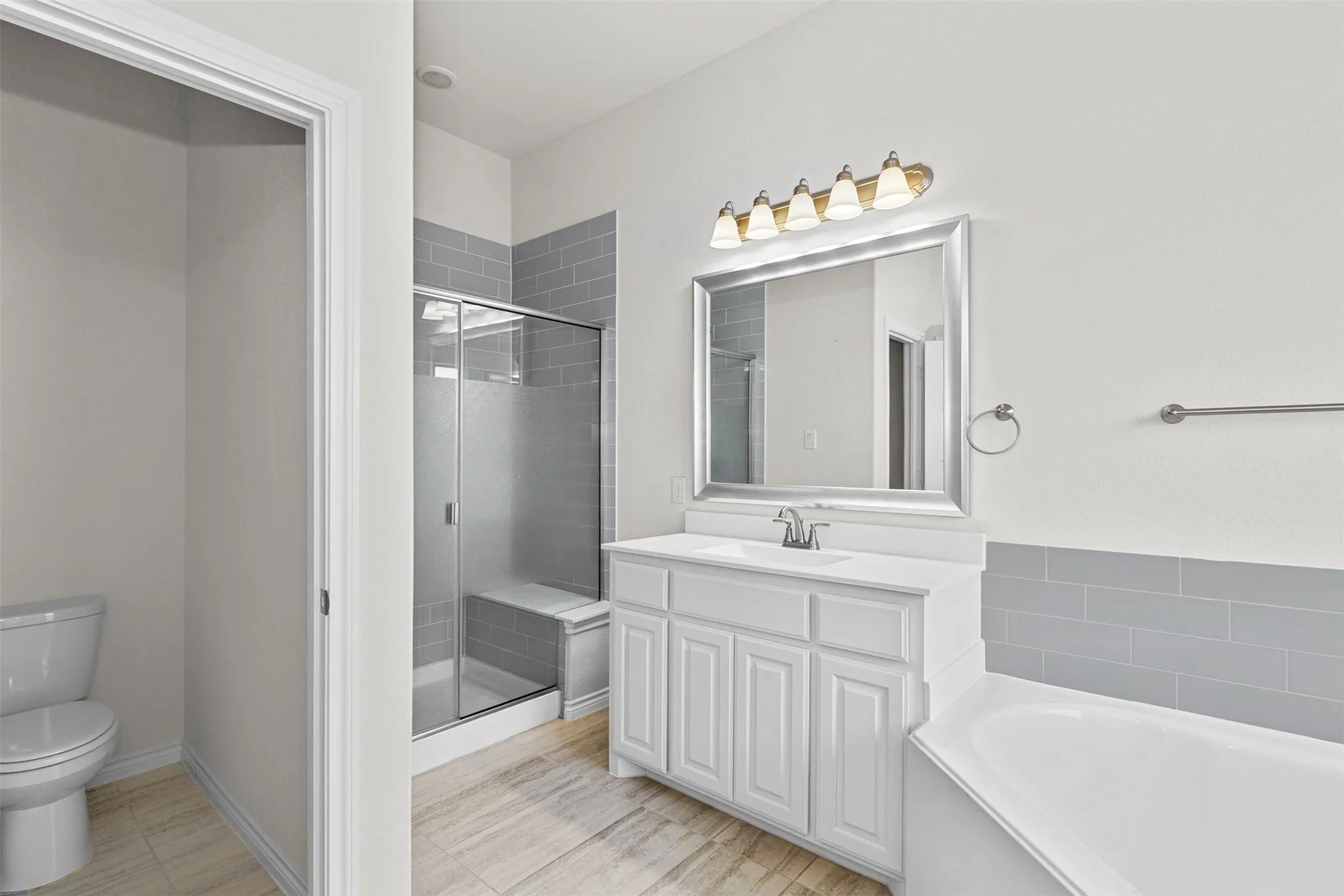 Spa-inspired primary bathroom featuring a white vanity with shaker-style cabinetry, a framed mirror with integrated lighting, and a separate soaking tub